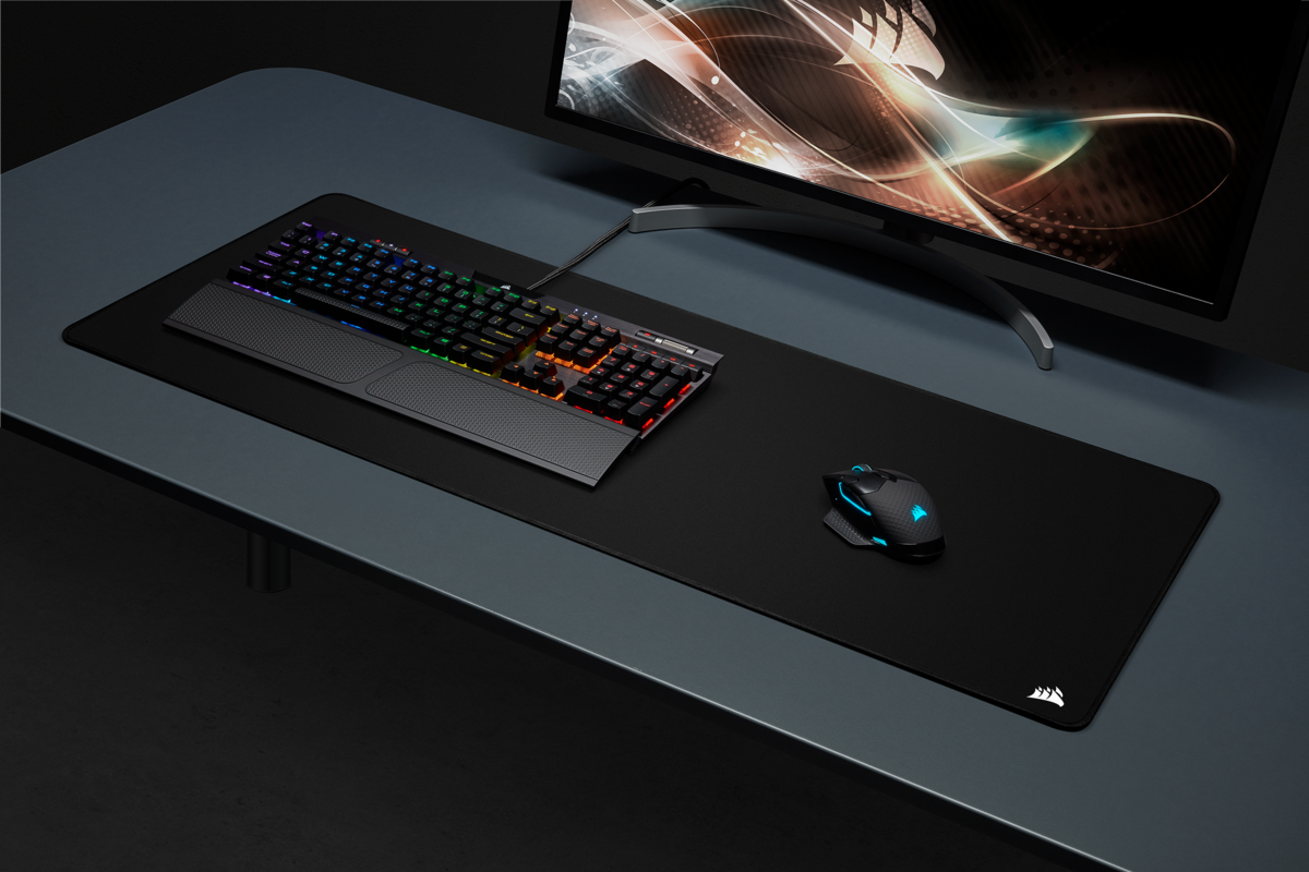 Configurazione gaming con tastiera, mouse e un grande tappetino su una scrivania scura.