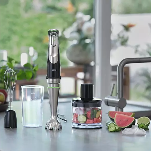 Comptoir de cuisine avec un mixeur et des fruits coupés, avec des plantes et une vue sur la fenêtre en arrière-plan.