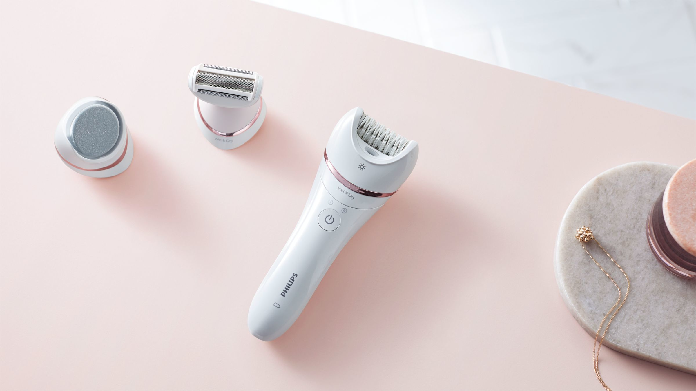 Drei weiße Philips Pflegegeräte auf rosa Oberfläche, mit einer Halskette.