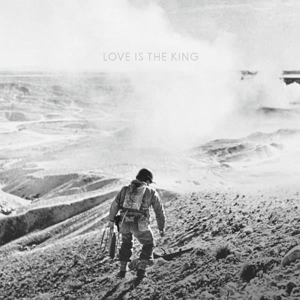 Soldat monte une colline en zone de guerre, portant de l'équipement, texte 'Love is the King', fond désert.