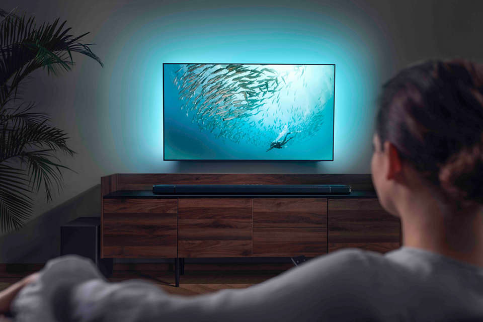 Eine Frau betrachtet einen Fernseher mit blauem Licht, einer Soundbar und einem Holzschrank.