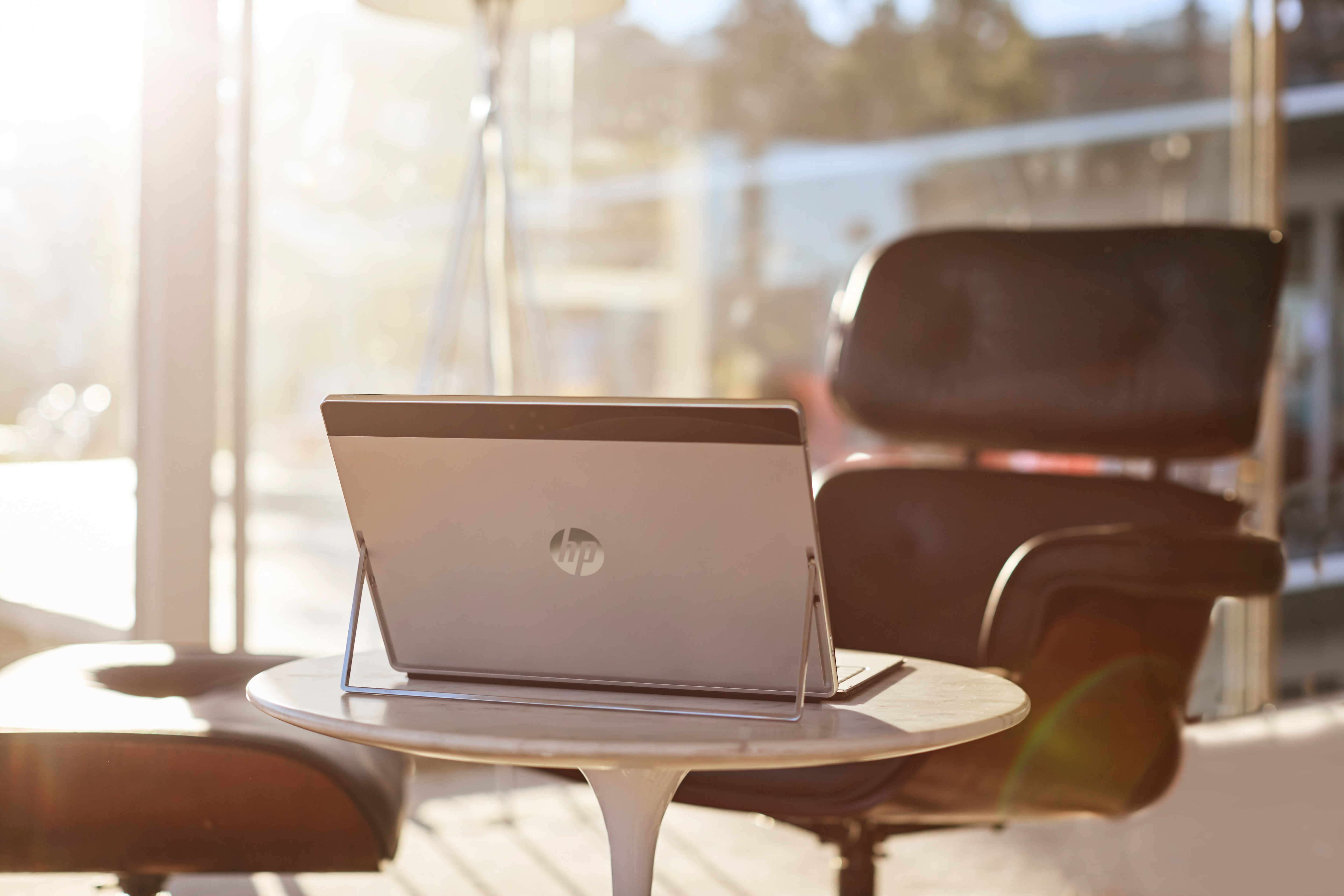 Ein HP Laptop steht auf einem runden Tisch in einem hellen, sonnigen Raum mit Sesseln im Hintergrund.