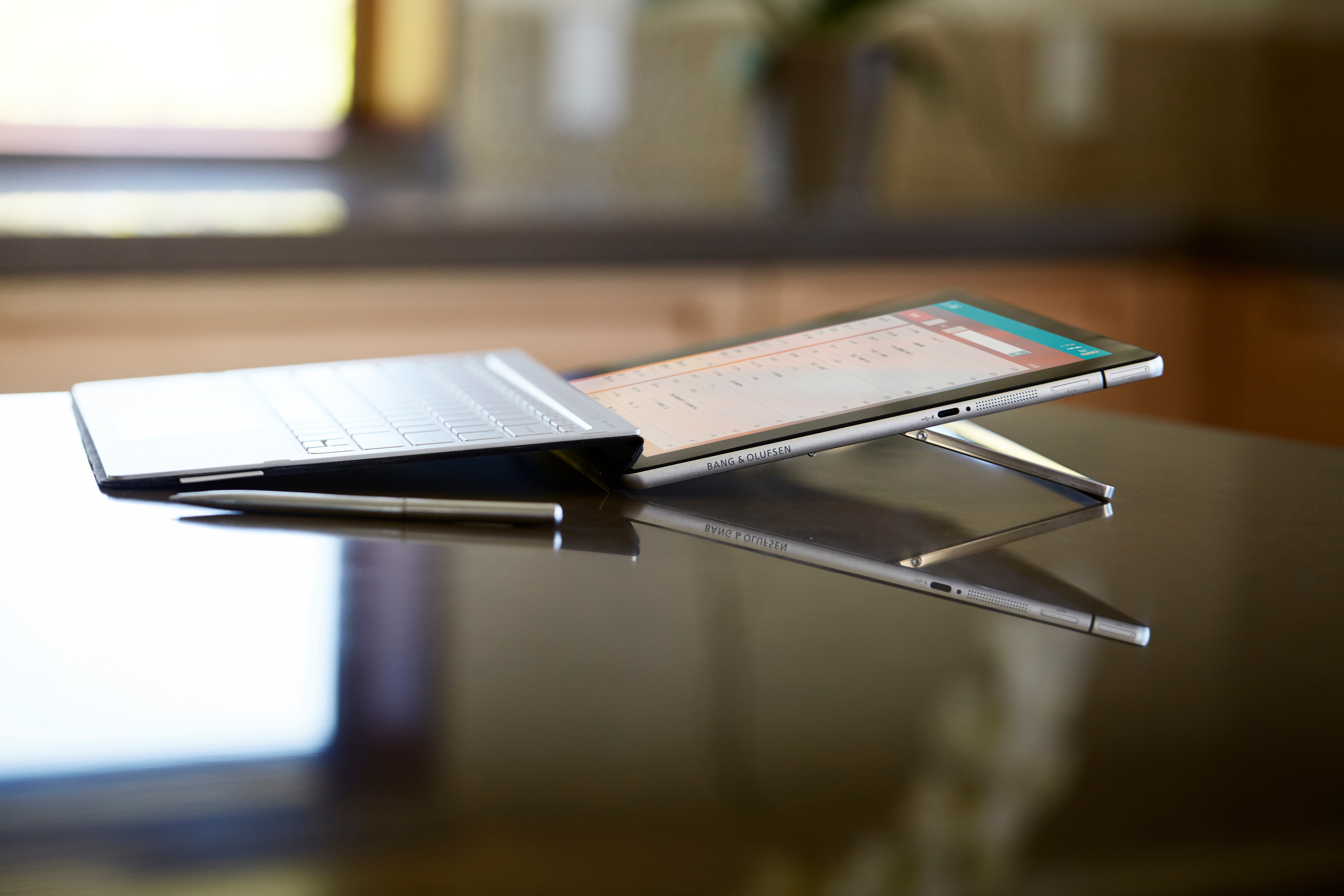 Ein Tablet mit Tastaturhülle und Eingabestift auf einem reflektierenden Holztisch.
