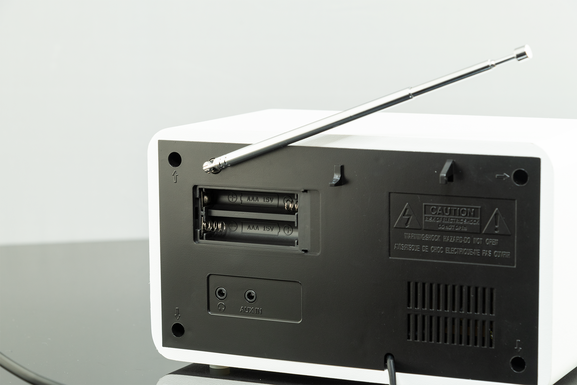 Rückseite eines weißen Radios mit Antenne, offenem Batteriefach und AUX IN-Anschluss.