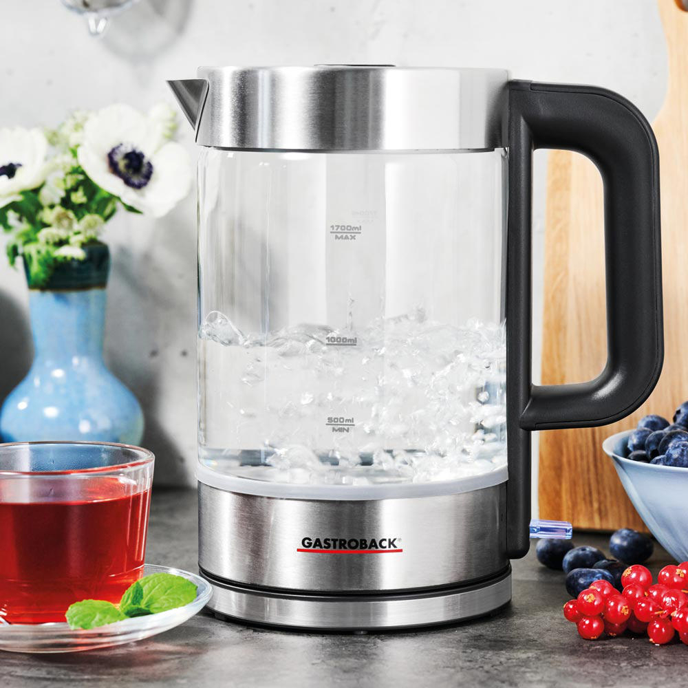 Elektrischer Glaskessel mit kochendem Wasser, roten Beeren, Blaubeeren und Teetasse mit Minze.
