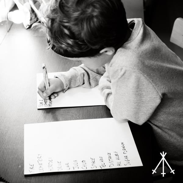 Ein kleiner Junge schreibt auf Papier, mit einer Wortliste, in einem Schwarzweißfoto.