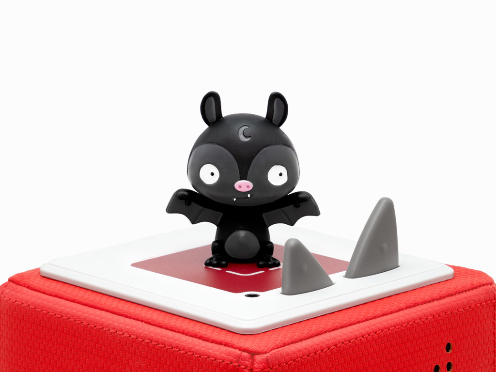 Ein schwarzes Fledermaus-Spielzeug mit Mond auf dem Kopf, stehend auf einem roten Block mit zwei grauen Haifischflossen.