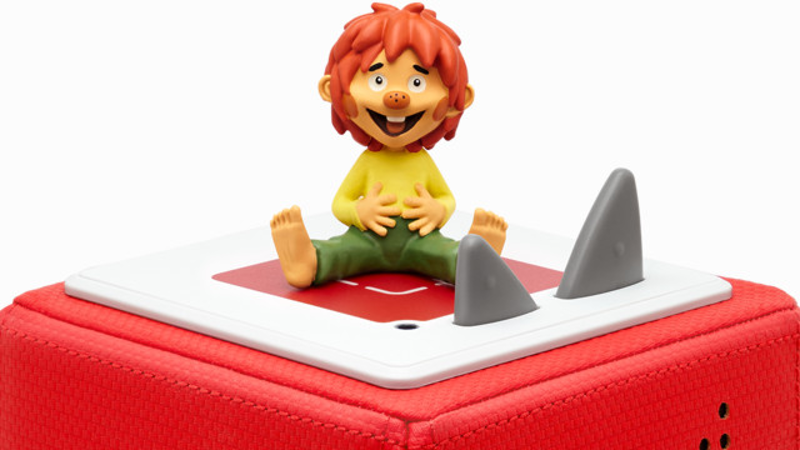 Eine Zeichentrickfigur sitzt auf einem roten Würfel mit zwei Haifischflossen. Es ist ein Kinderspielzeug.