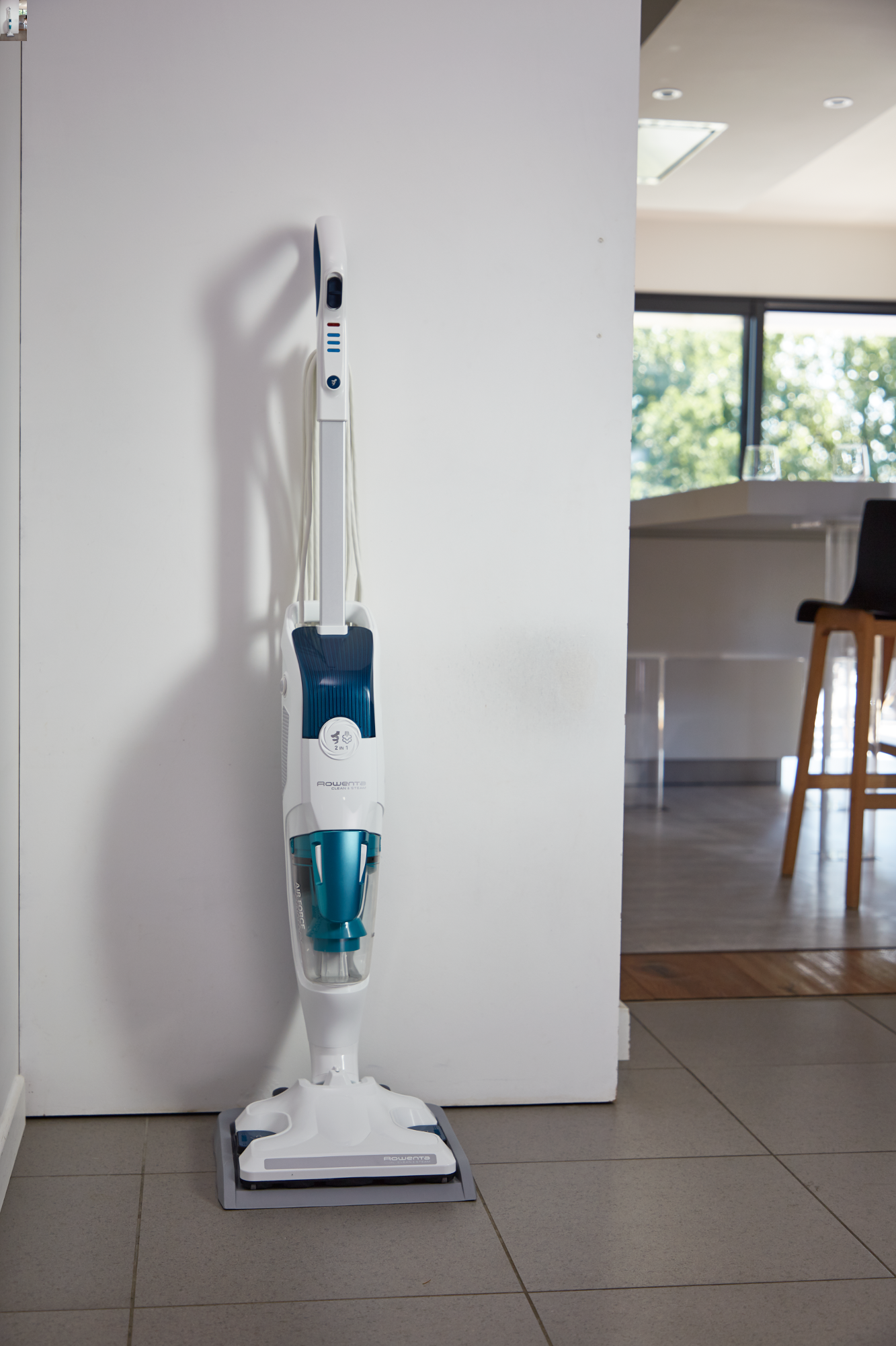 Un balai vapeur blanc et bleu est appuyé contre un mur blanc.