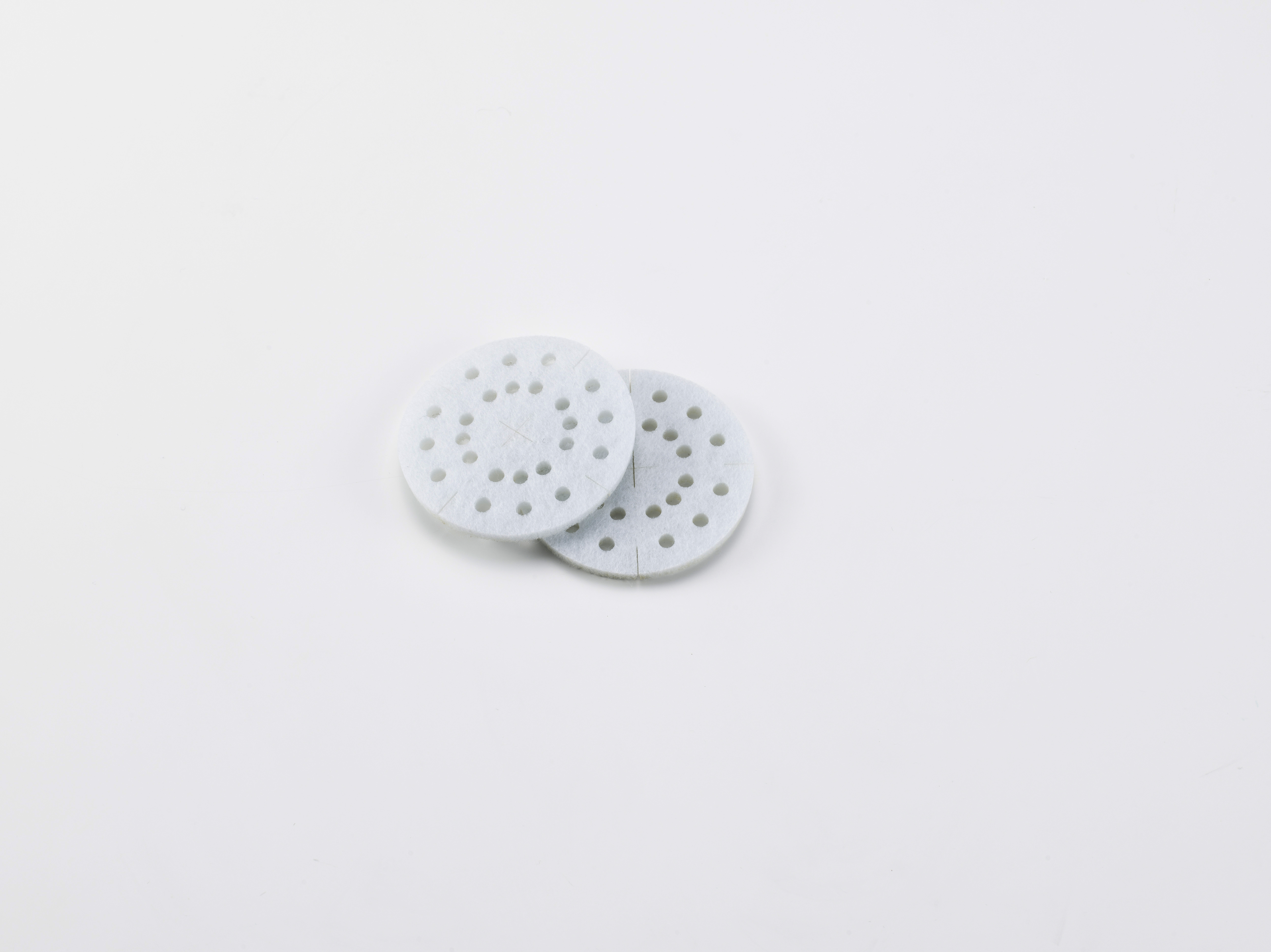 Zwei weiße, kreisförmige Schleifpads mit kleinen Löchern, auf weißem Hintergrund.