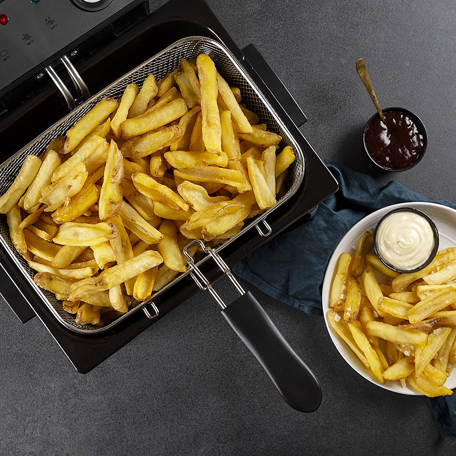 Frittierte Pommes in einem Korb und ein Teller mit Mayo. Dunkler Hintergrund.
