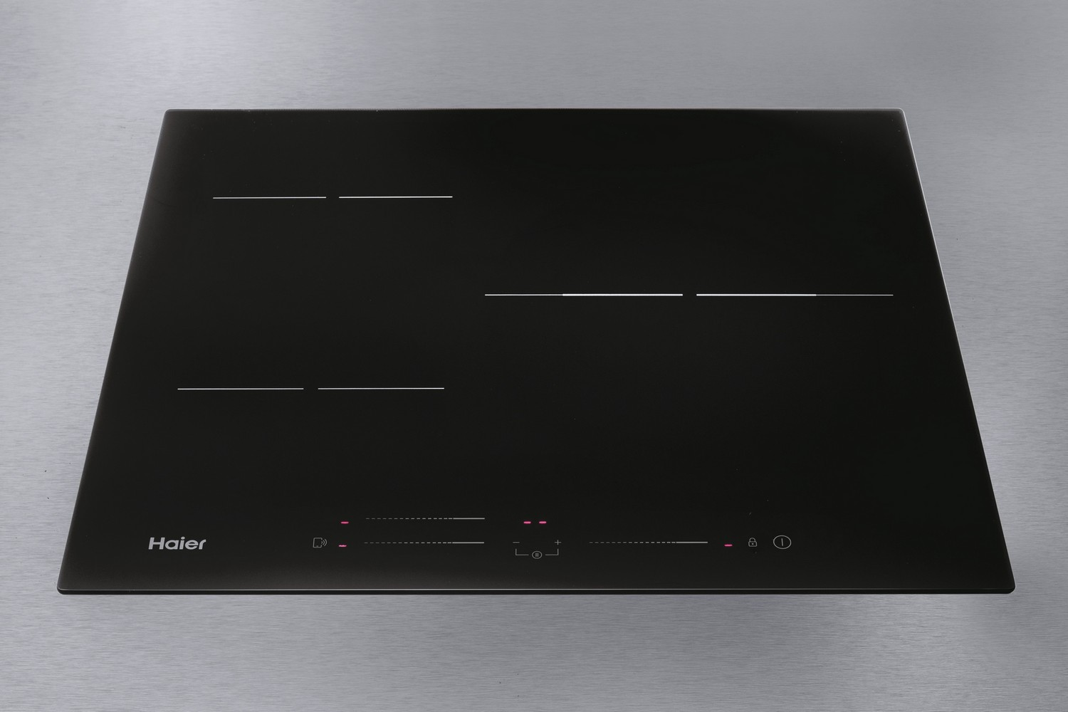 Una placa de inducción Haier negra sobre una superficie plateada con cuatro zonas de cocción.