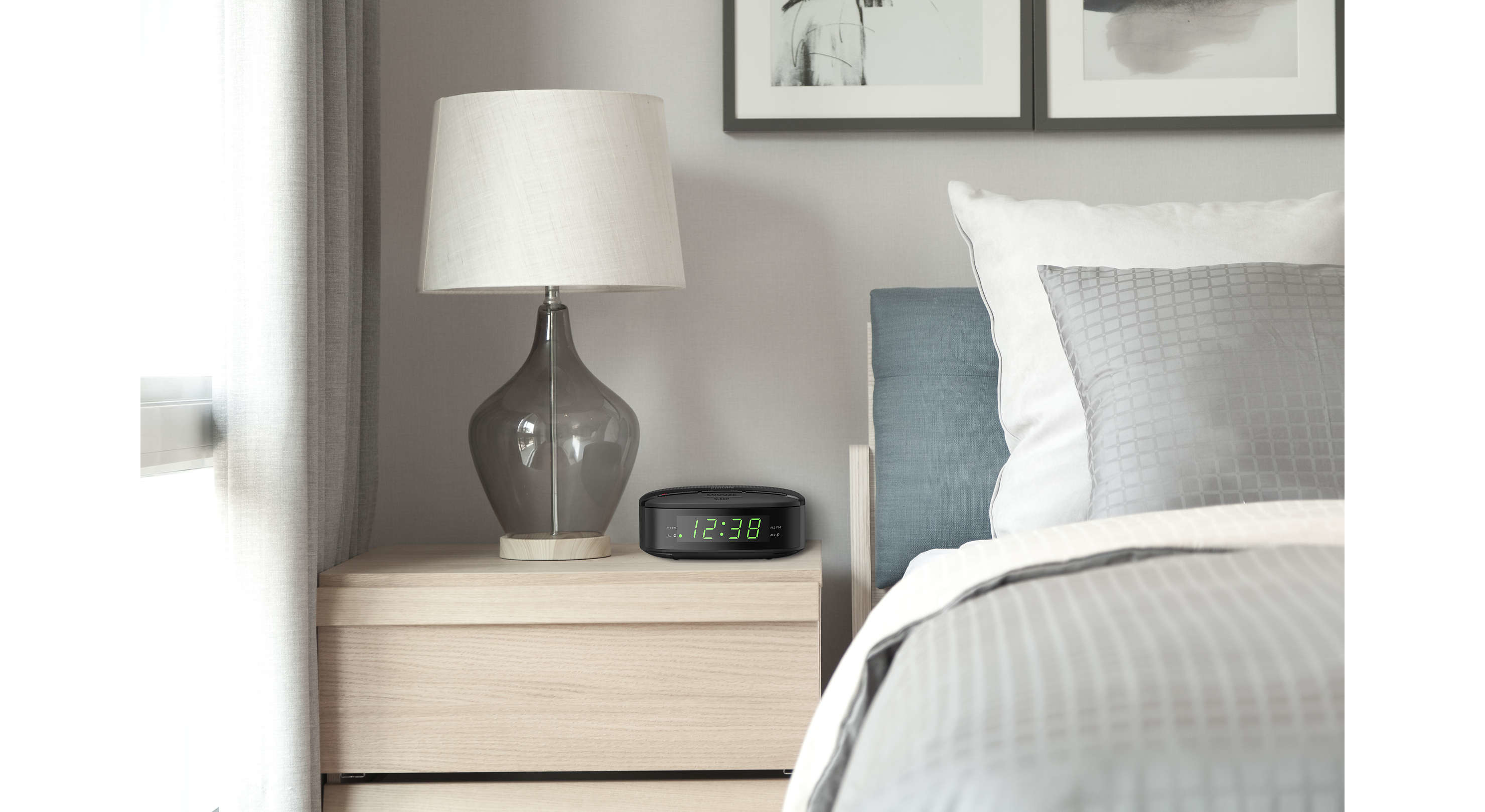 Bedroom scene: bedside table with a lamp and clock. Bed with pillows and comforter.