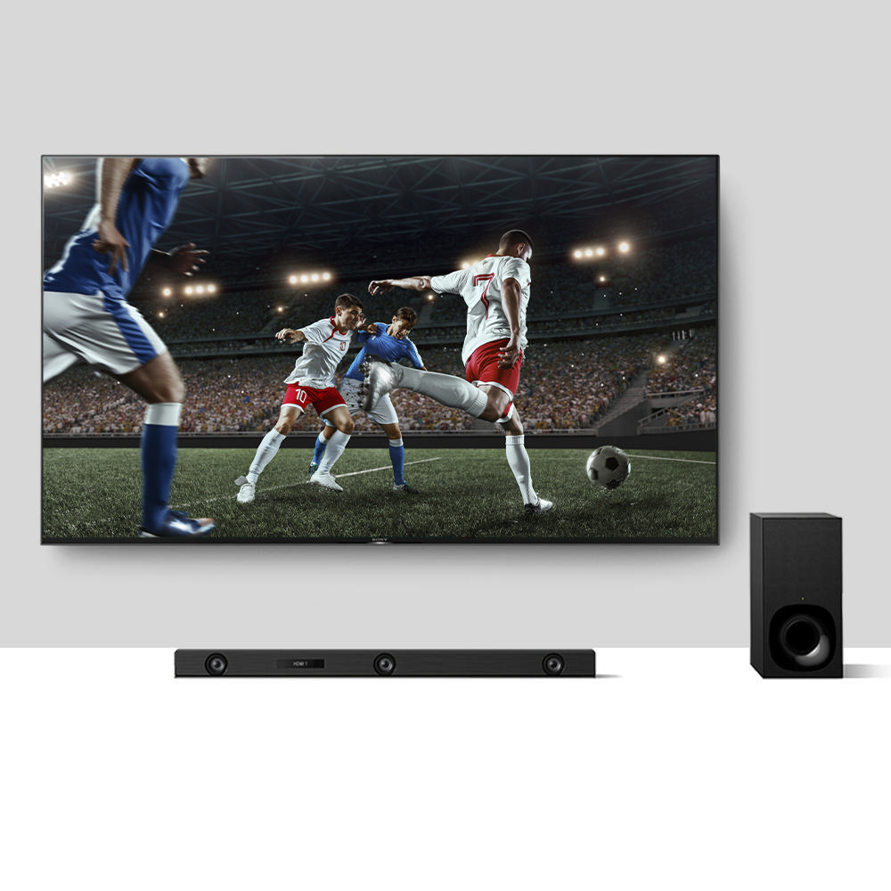 Ein Fernseher zeigt ein Fußballspiel. Eine Soundbar und ein Subwoofer befinden sich unter dem Bildschirm.