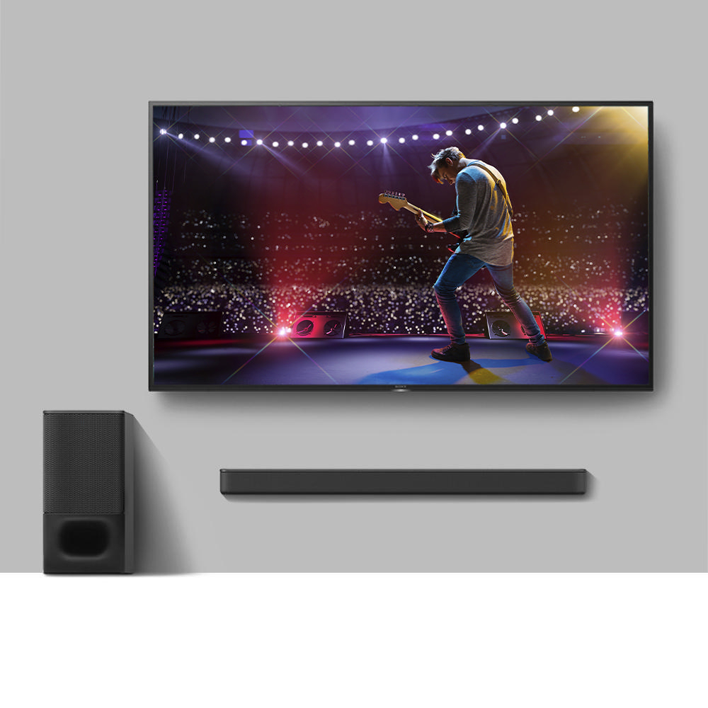 Ein Fernsehbildschirm, der einen Mann zeigt, der auf der Bühne Gitarre spielt, mit einer Soundbar.