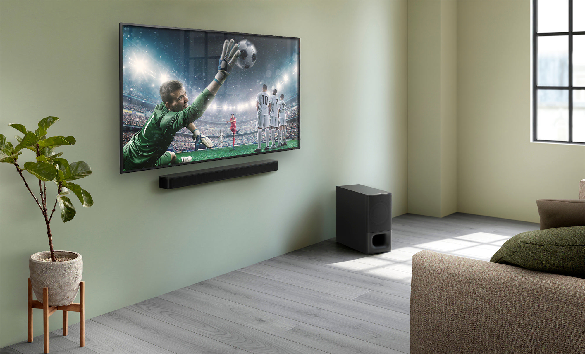 Wohnzimmer mit Fernseher, der ein Fußballspiel zeigt. Unter dem Fernseher befindet sich eine Soundbar. Rechts ein Subwoofer.