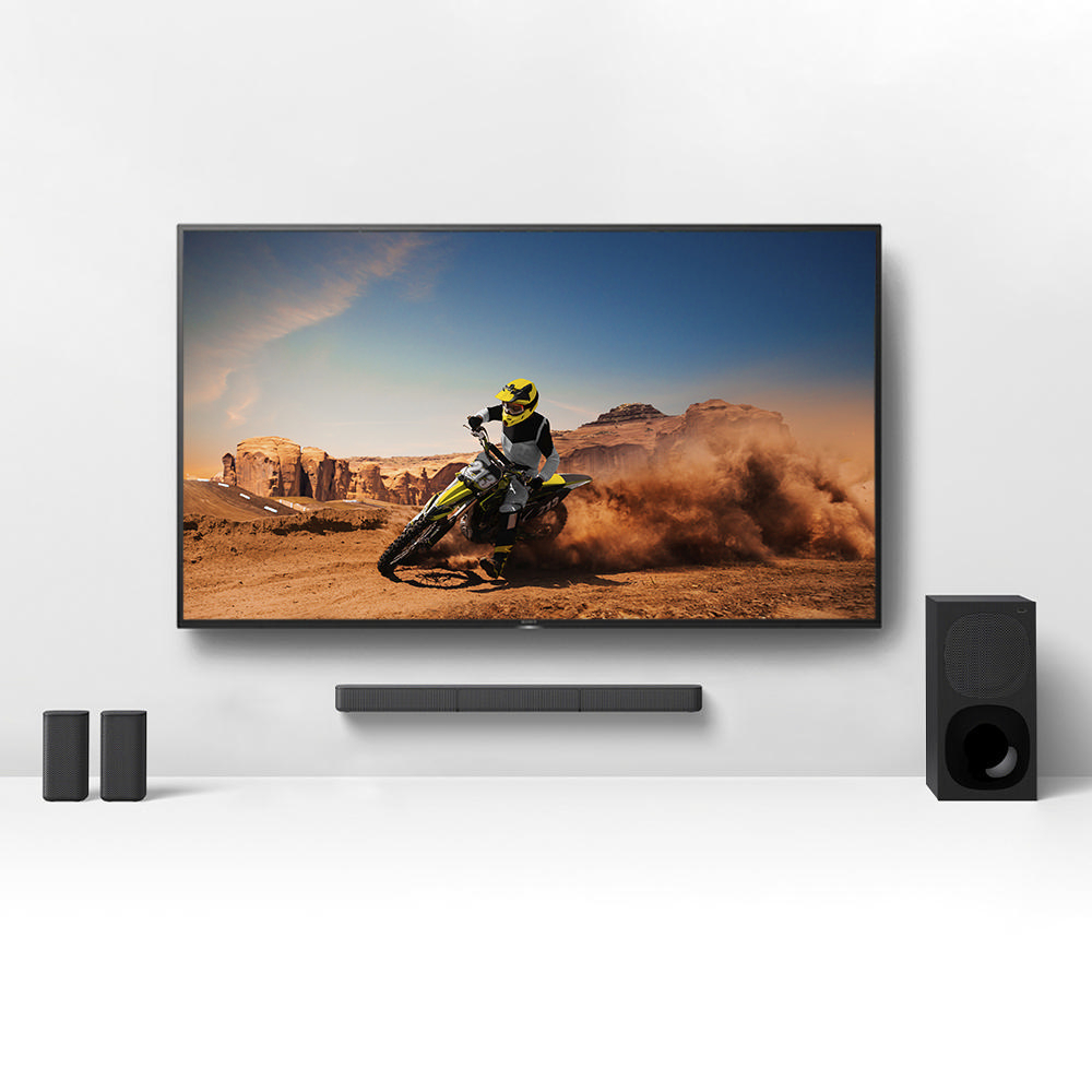 Fernseher zeigt Motocross-Rennen, Soundbar und zwei kleine Lautsprecher.