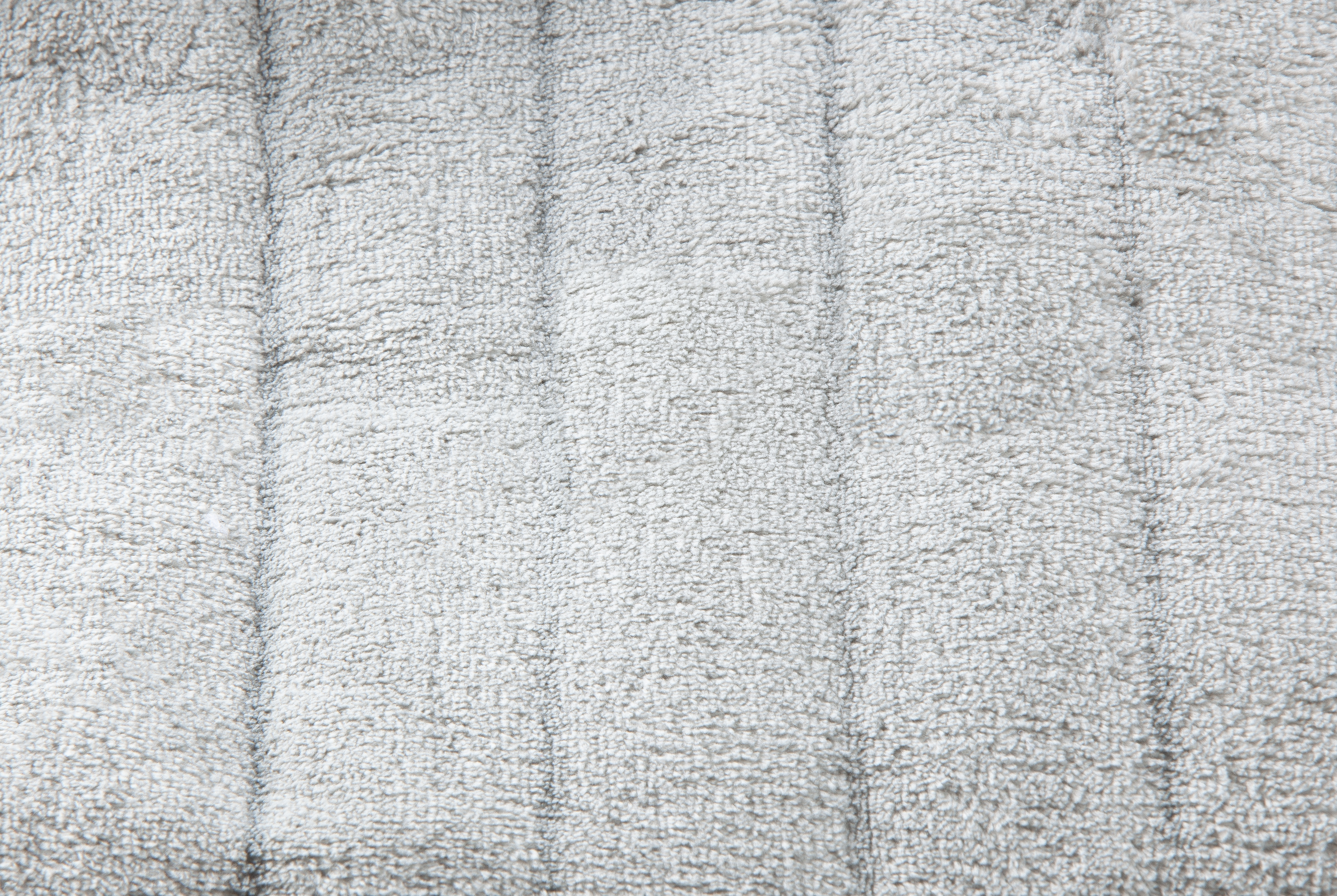 Close-up of a grey, textured surface with vertical lines. It appears to be fabric.