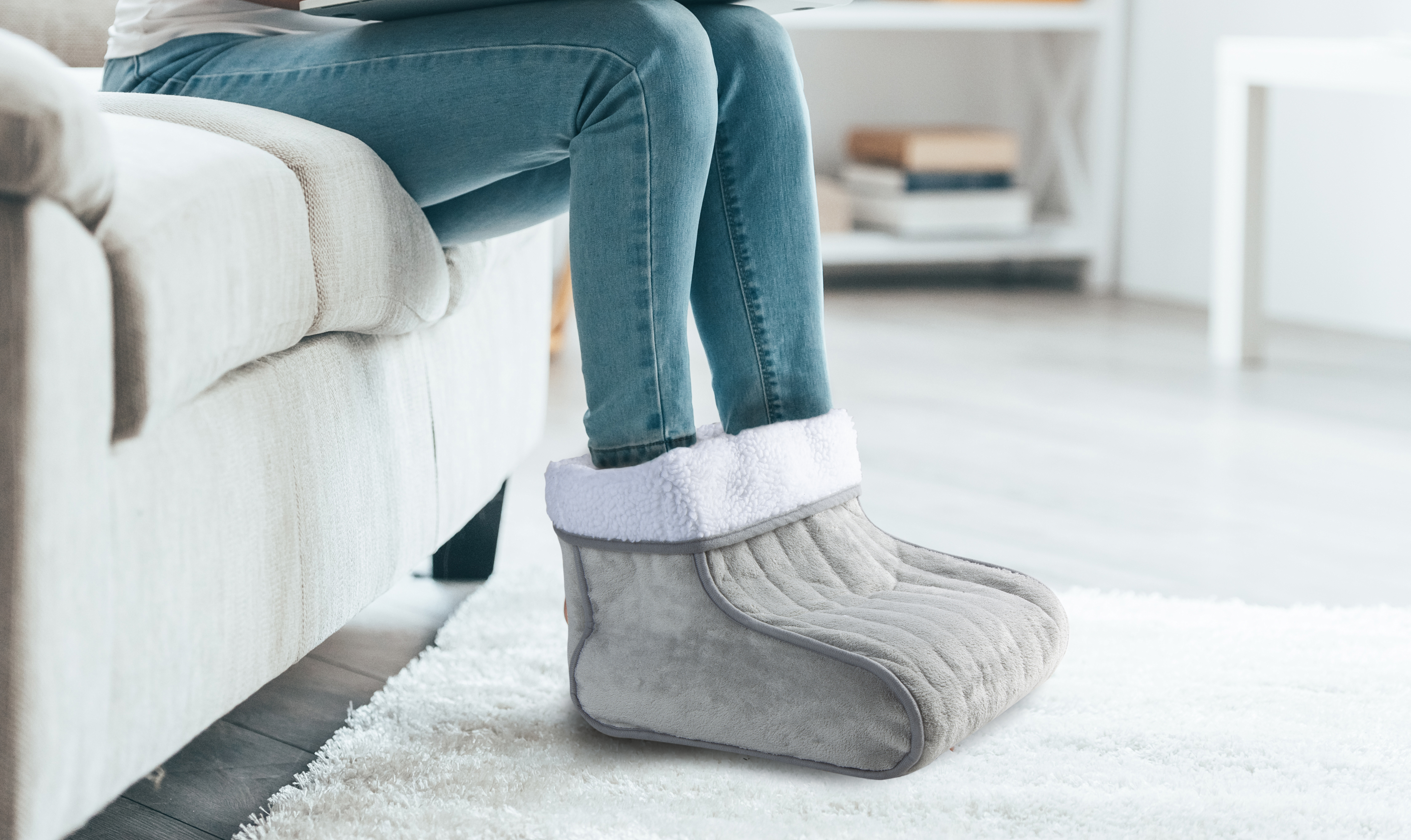 Person wearing cozy gray foot warmers, sitting on a sofa, with a laptop.