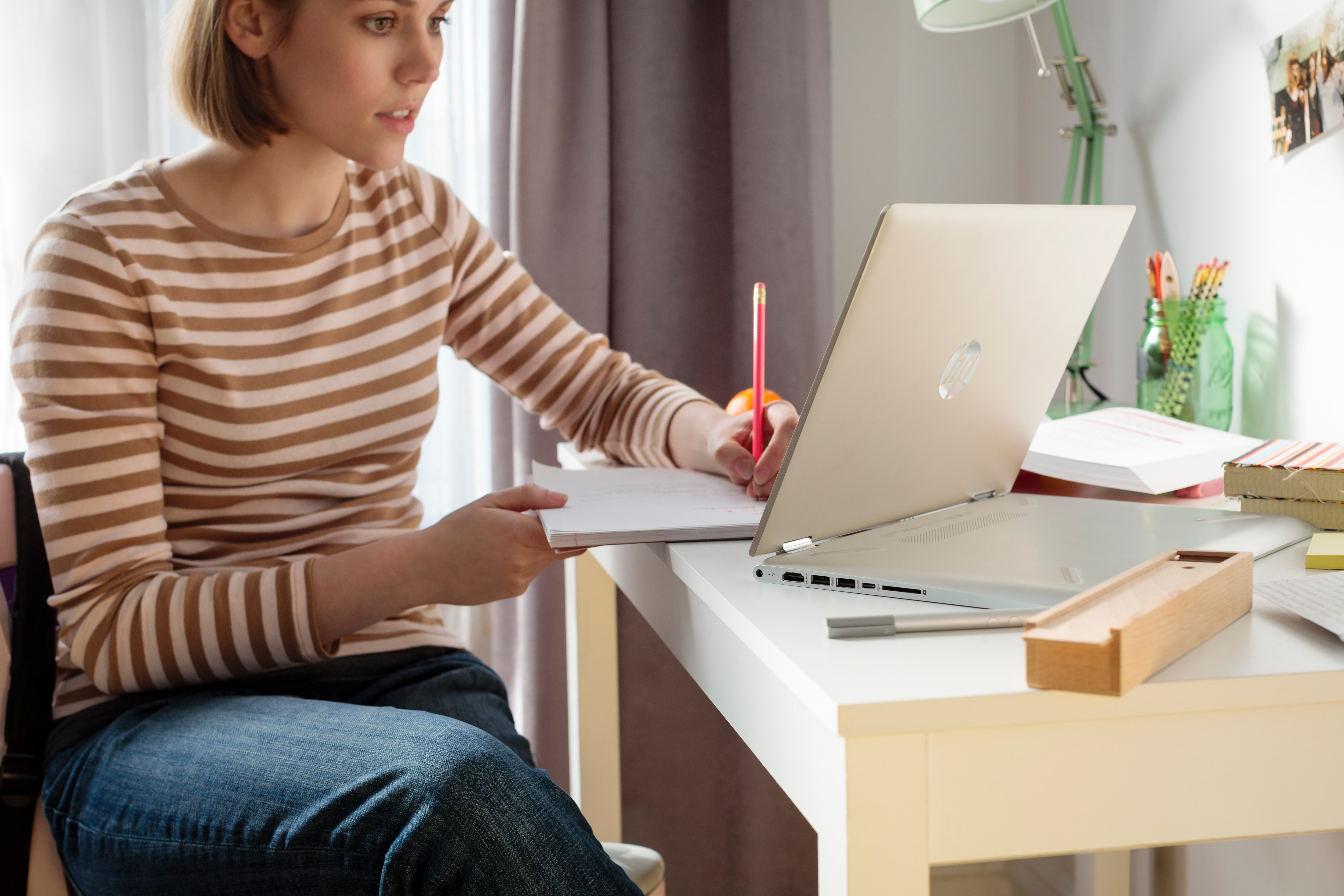 Frau mit gestreiftem Oberteil sitzt an weißem Schreibtisch vor Laptop und schreibt in Notizbuch.