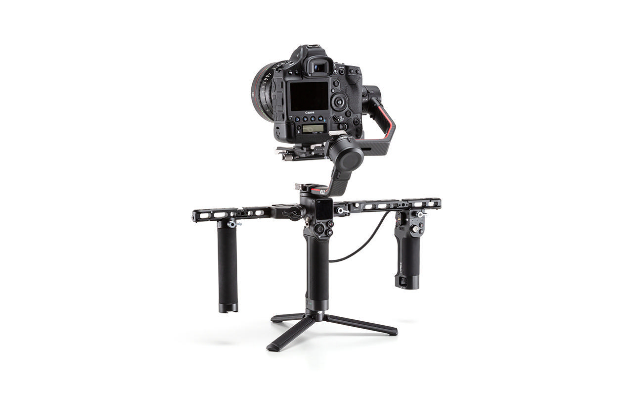 Schwarze Kamera auf Gimbal-Stabilisator mit Griffen, auf Stativ, vor weißem Hintergrund.