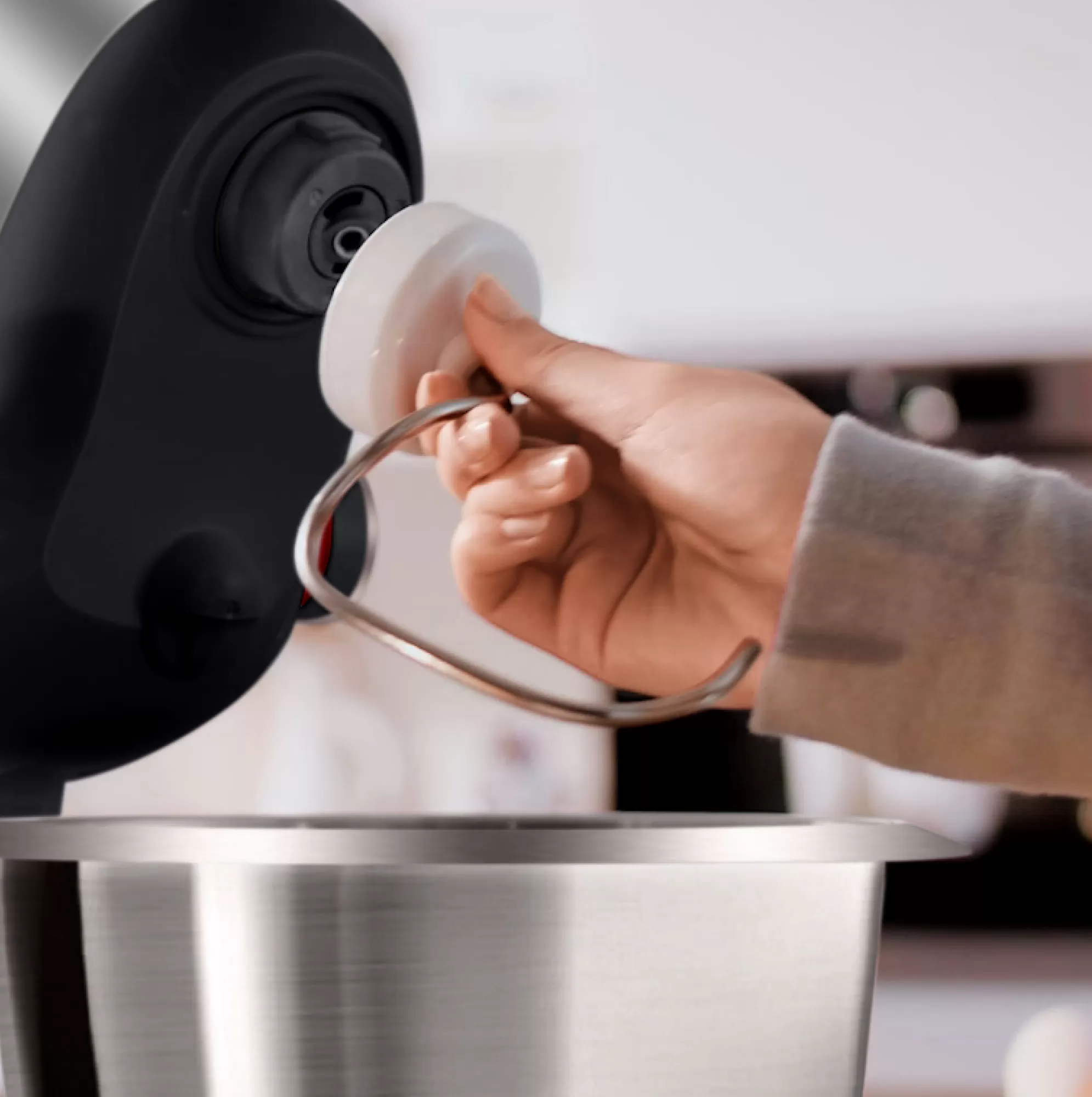 Een hand plaatst een deksel op de haakbevestiging van een mixer. De mixer is zwart en zilver.