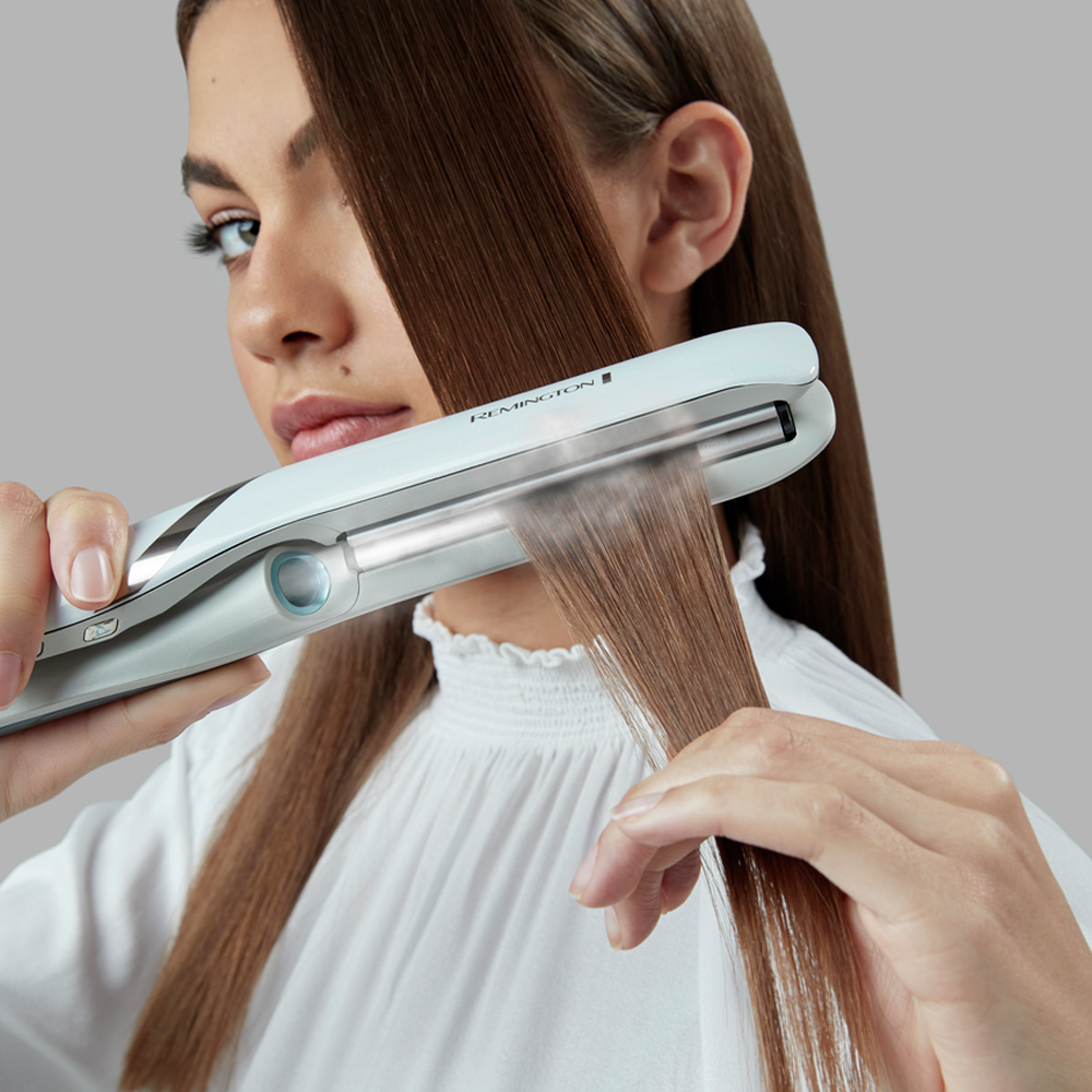 Woman using a hair straightener, straightening brown hair.