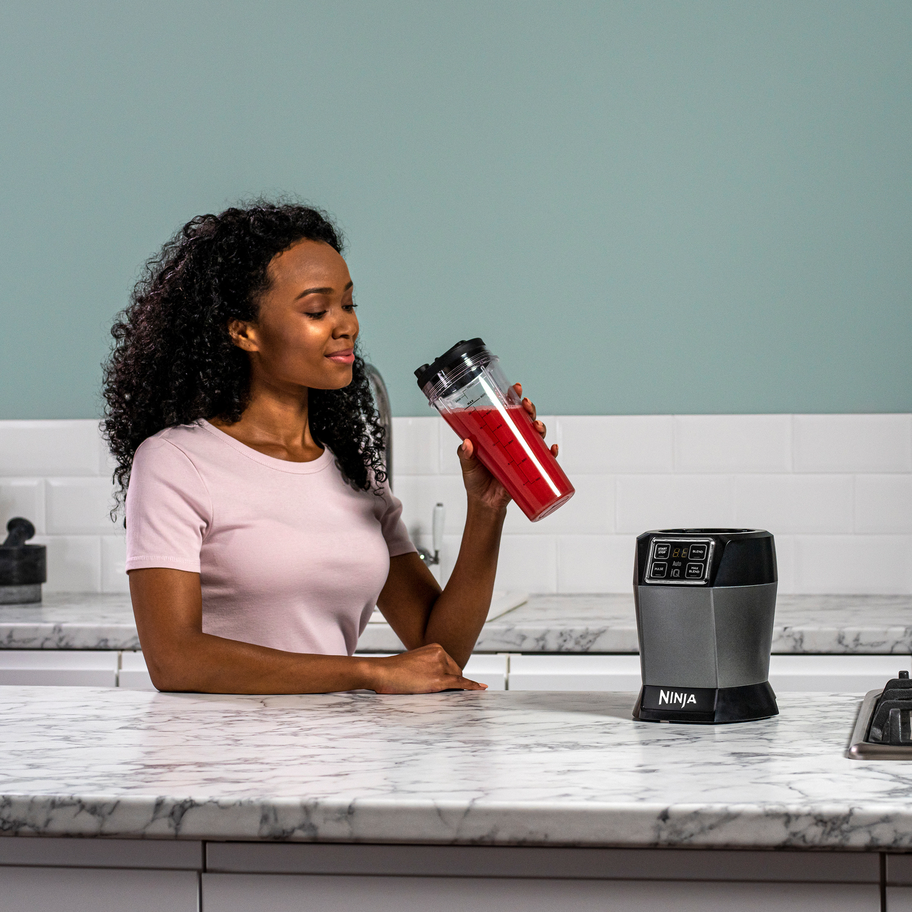 Une femme tenant un gobelet de mixeur avec un liquide rouge, près d'une base de mixeur.