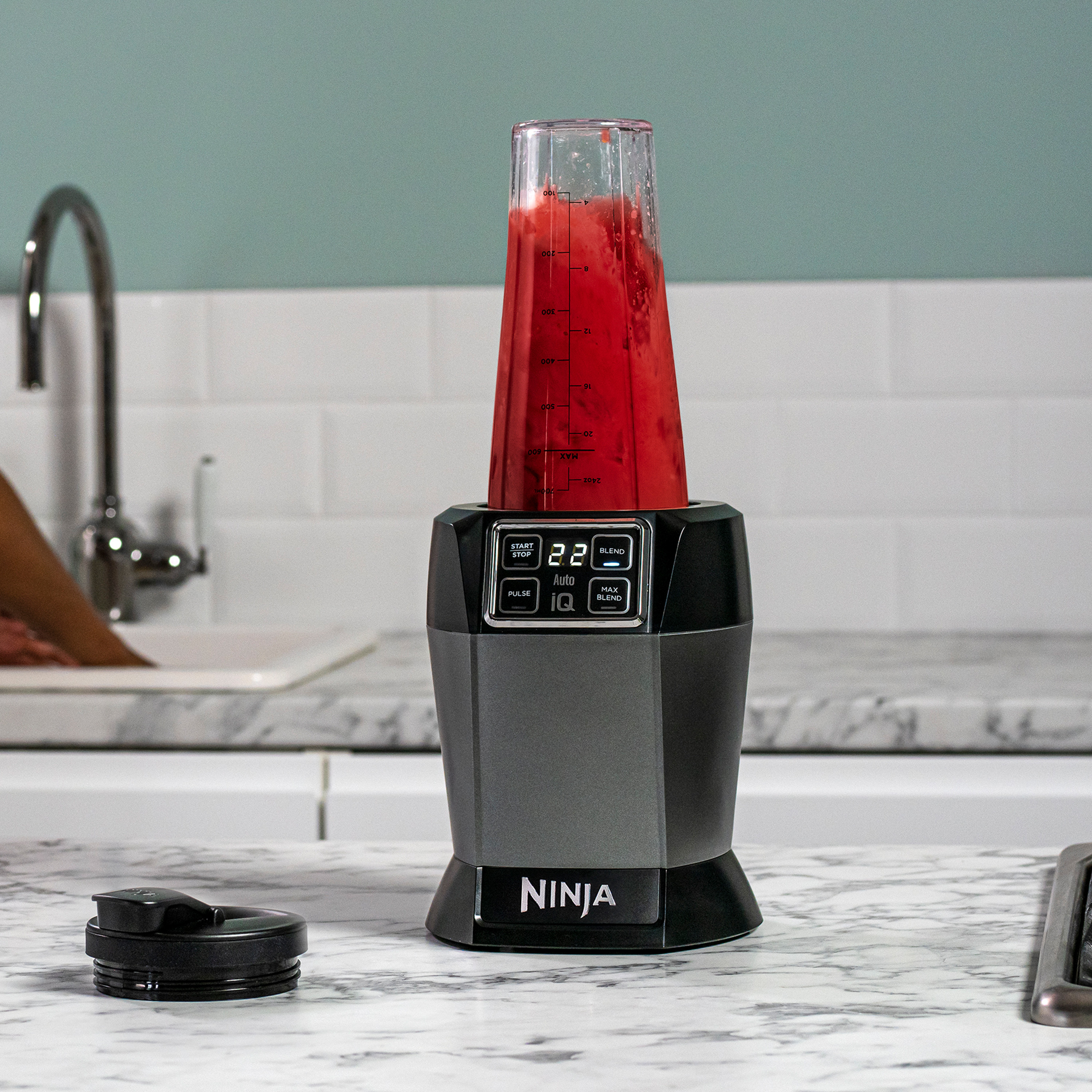 Mixeur Ninja noir et gris avec un liquide rouge dans un récipient transparent, sur une surface blanche.