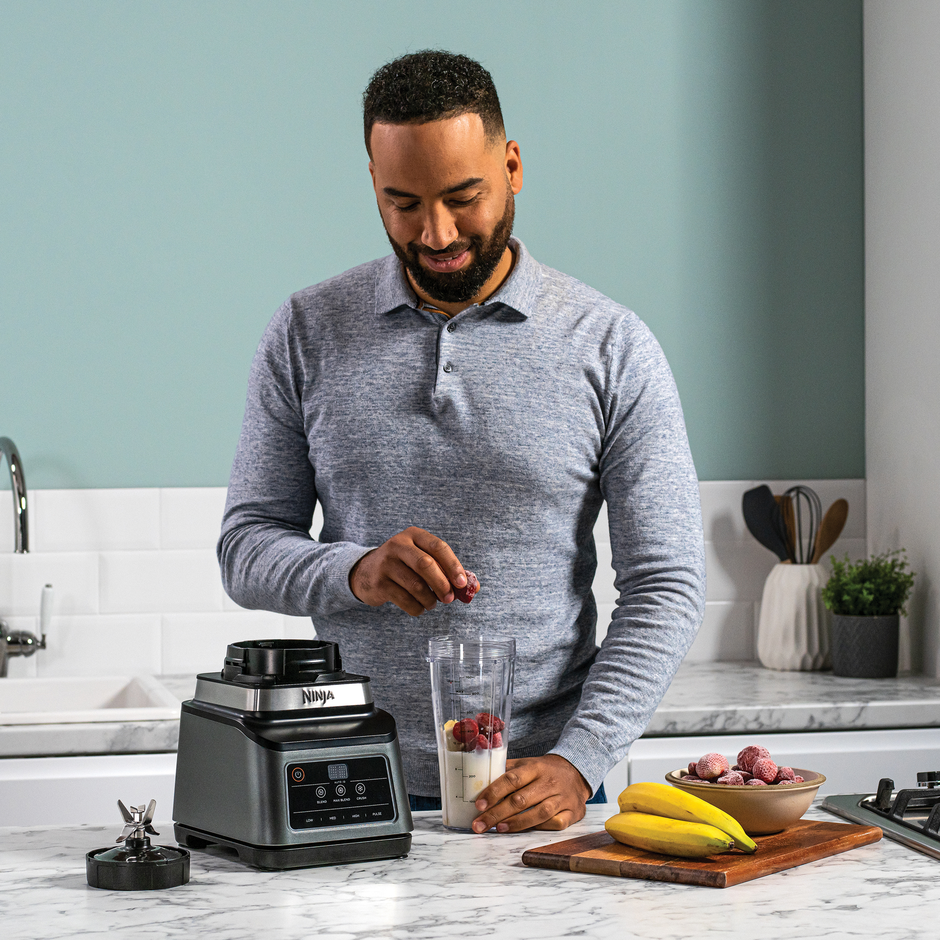A man adding fruit to a blender, with ingredients and a countertop.