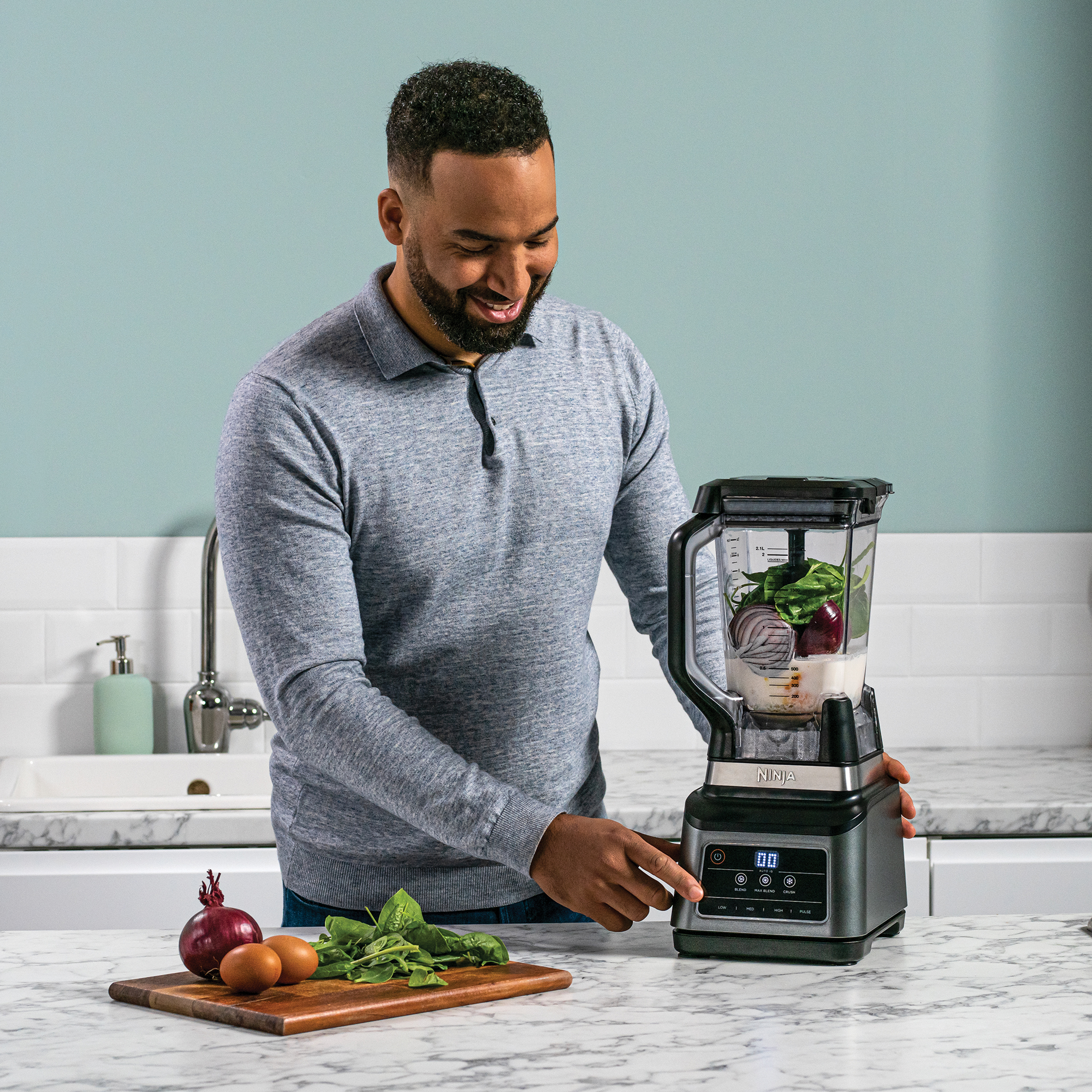 Man preparing ingredients for blender. Red onion, spinach, and eggs on the counter.