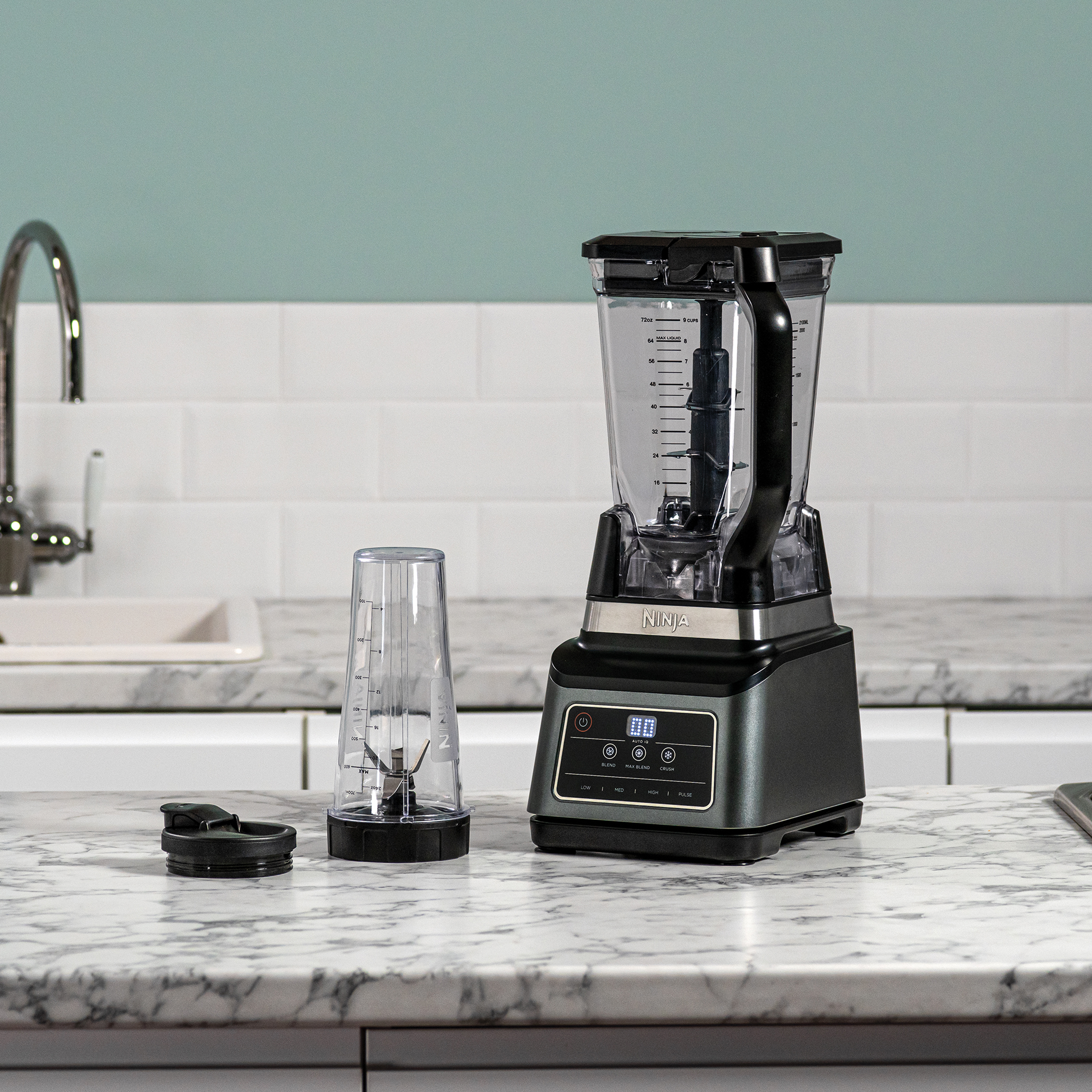 Black and silver Ninja blender with accessories on a marble countertop. White backsplash and wall.