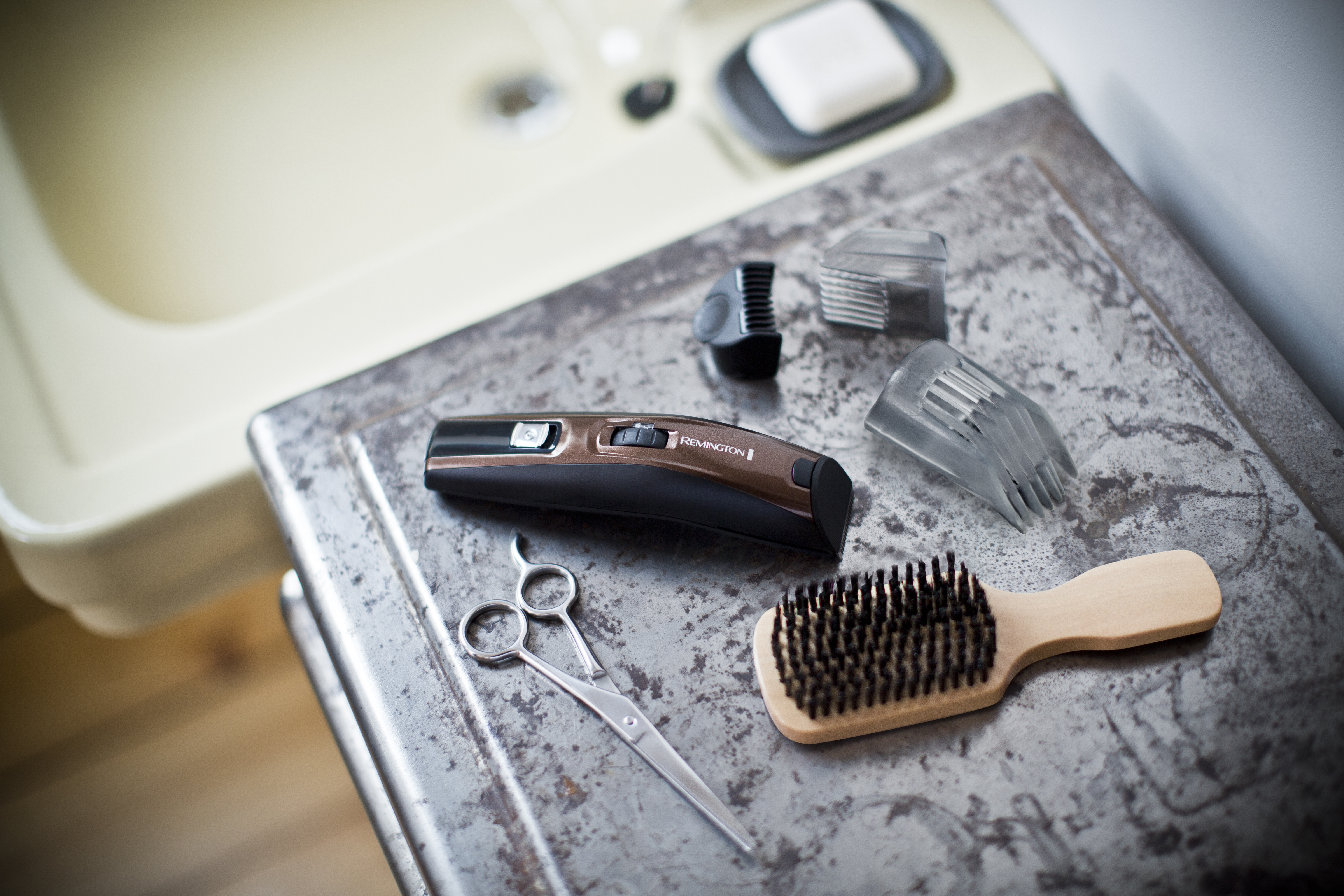 Grooming tools including a trimmer, scissors, combs and a brush, arranged on a metal surface.