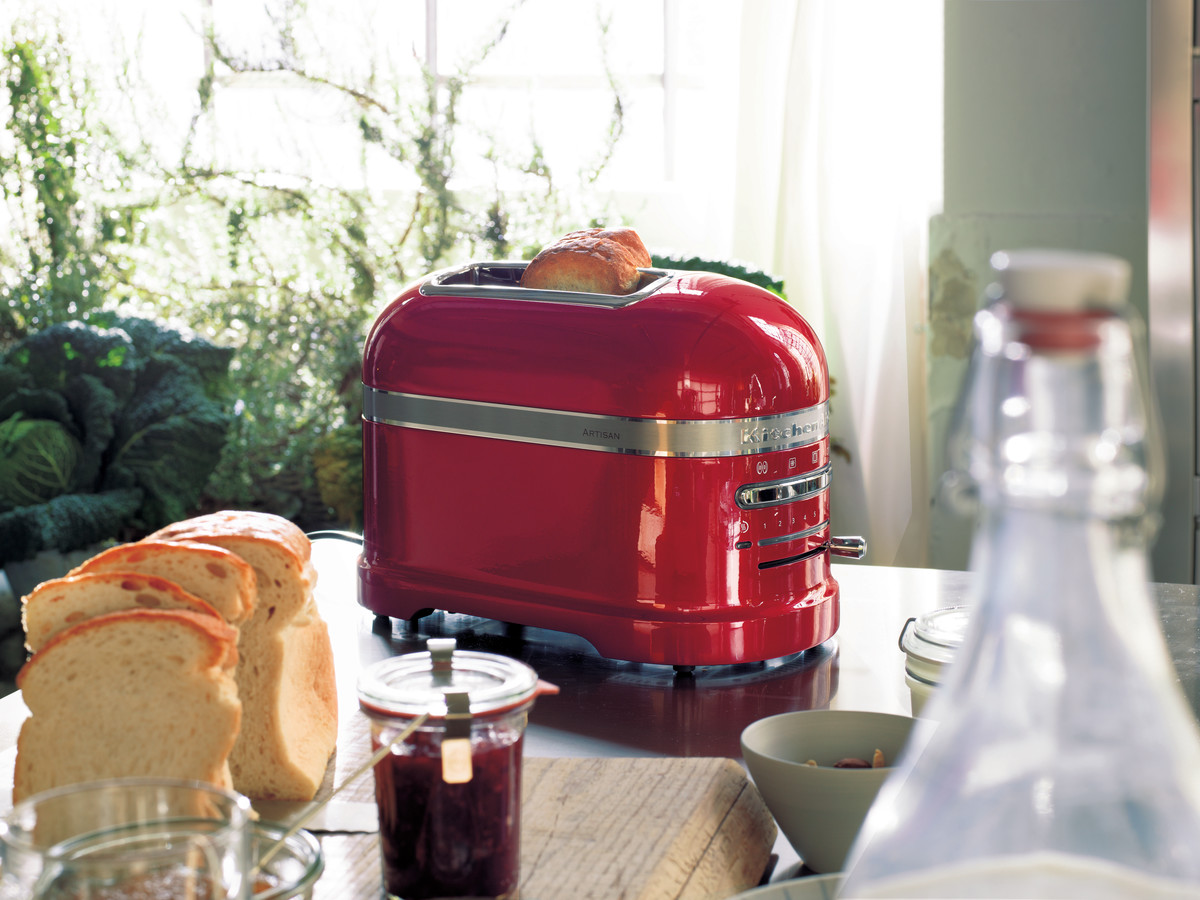 Roter KitchenAid Toaster mit Toast. Brotscheiben und Marmeladenglas stehen auf dem Tisch.
