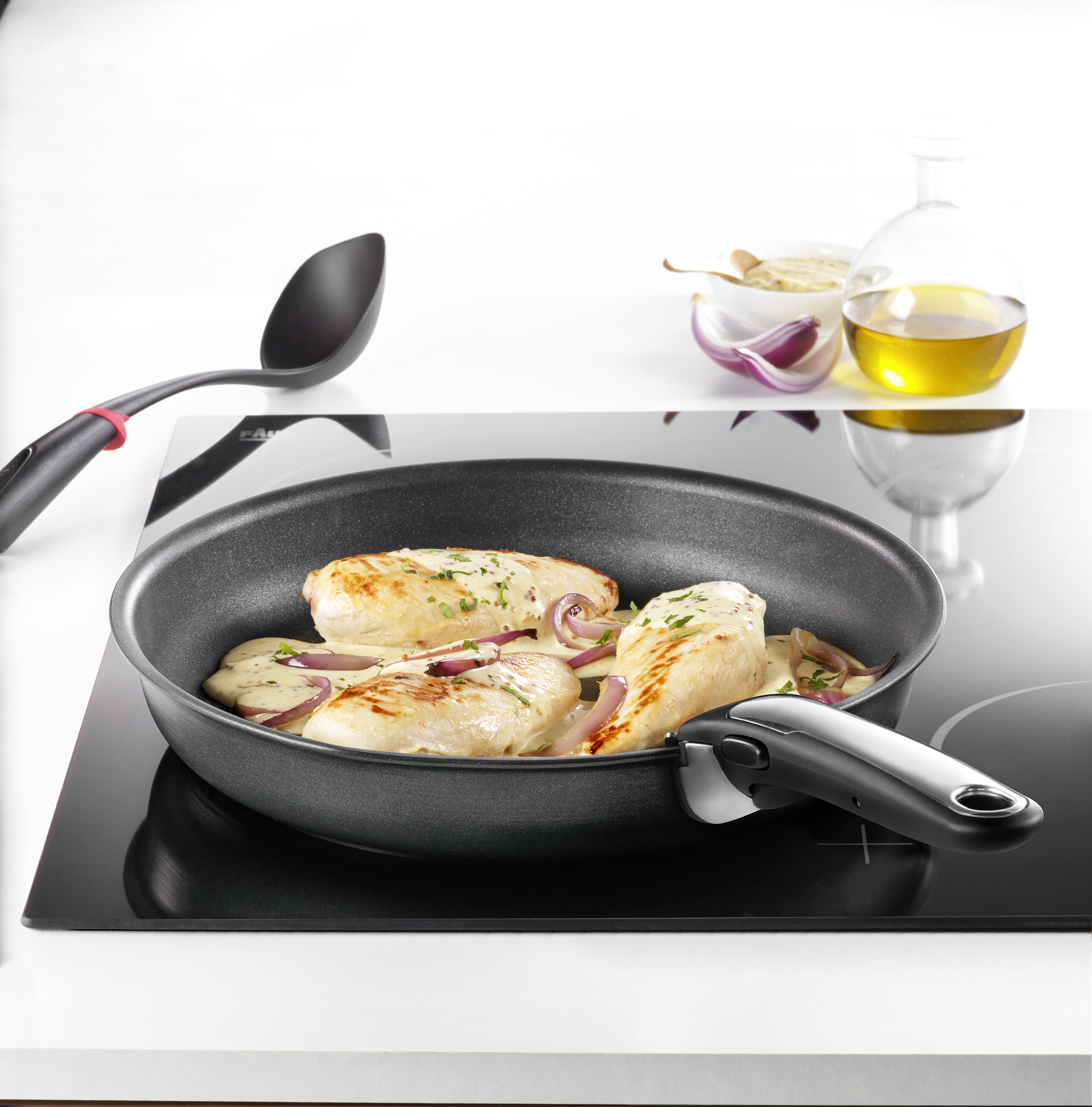 Poitrines de poulet dans une poêle avec oignons et sauce. Une cuillère, une bouteille d'huile et des ingrédients sont en arrière-plan.