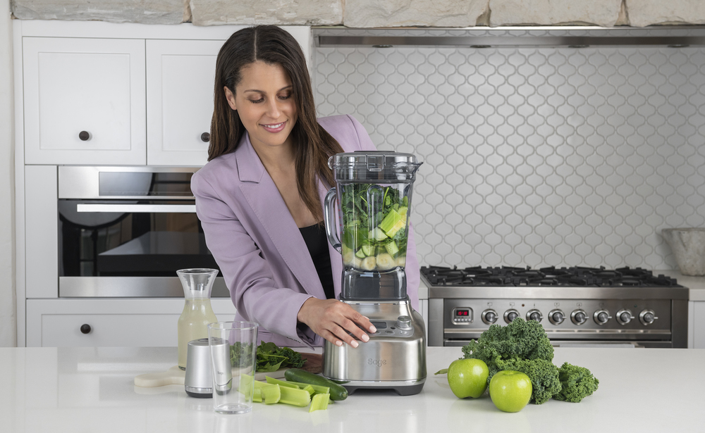 Nő a konyhában smoothie-t készít. Van egy turmixgépe és hozzávalók a pulton.