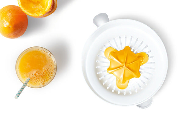 Orangensaft im Glas mit Strohhalm, Orangenhälften und Saftpresse auf weißer Oberfläche.