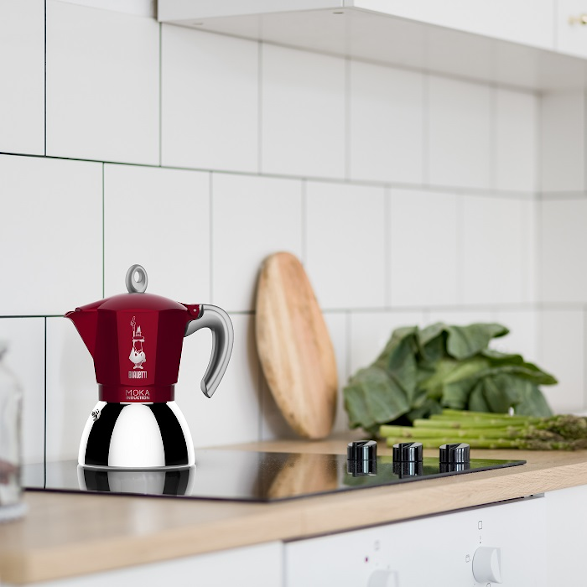 Piros Bialetti Moka kávéfőző fekete főzőlapon, fehér csempés háttérrel.