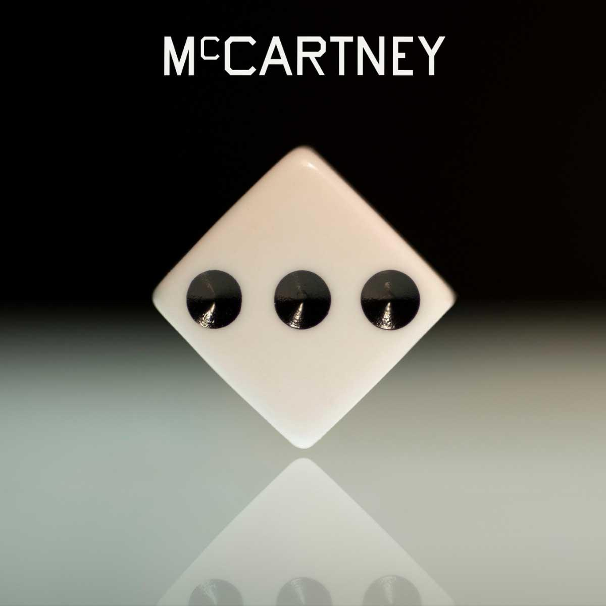 Witte dobbelsteen met drie zwarte stippen. McCartney staat erboven.