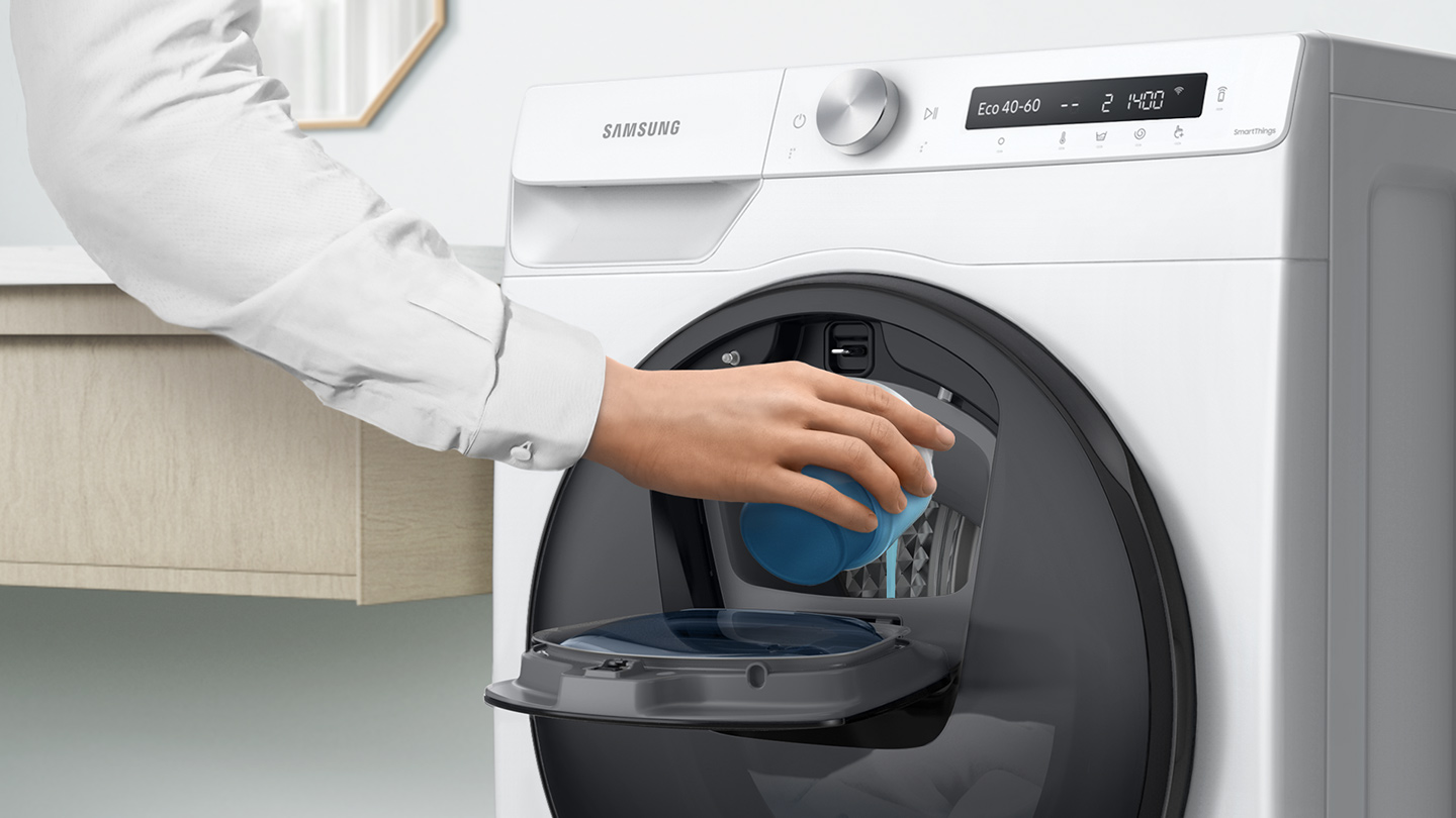 Een hand giet blauwe vloeistof in een wasmachinelade. Witte machine.