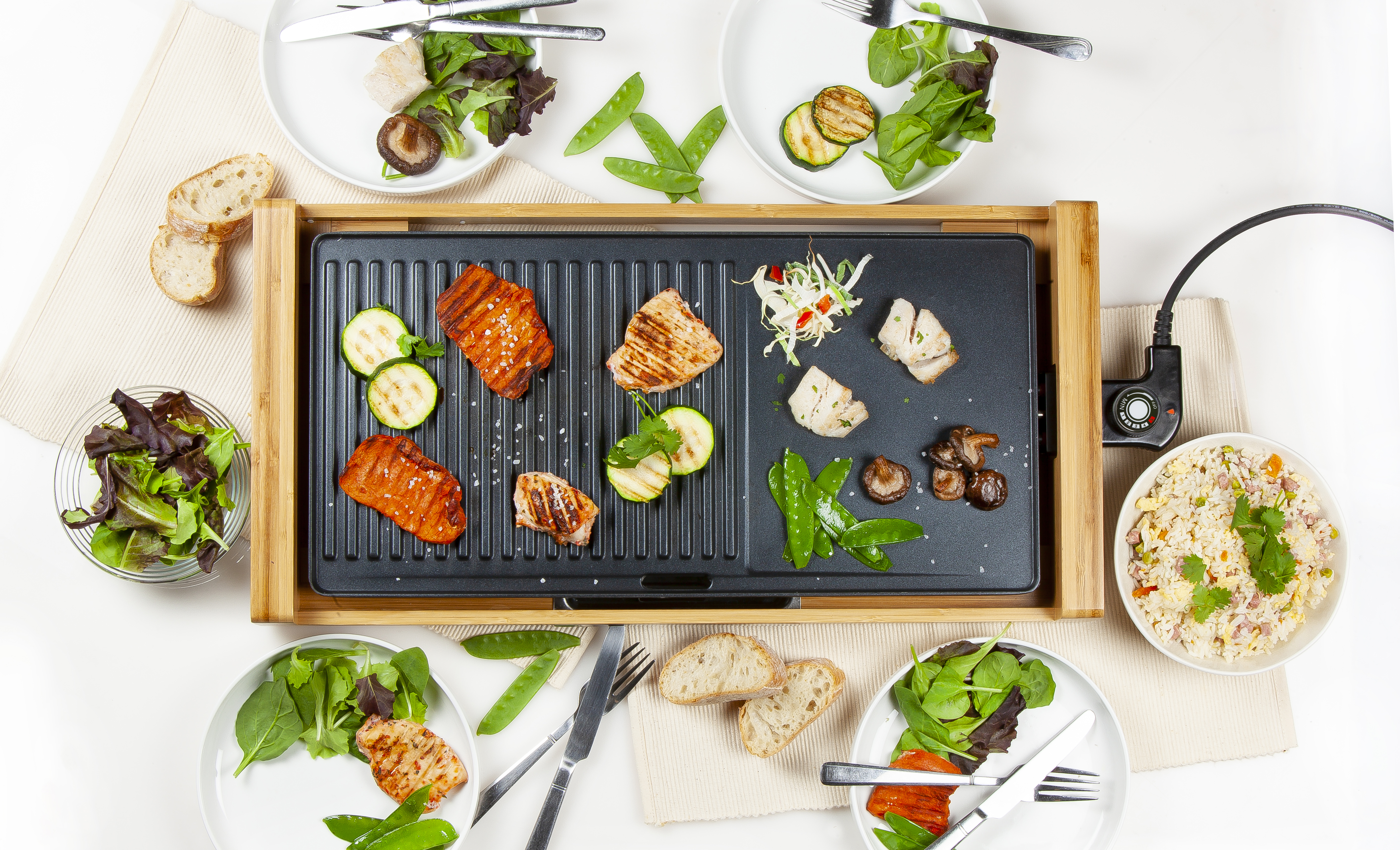 Overhead shot of food on a grill, plates with salads, and rice.