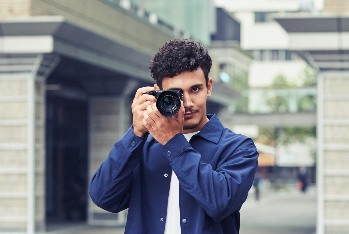 Een man in een blauw jasje die een foto maakt met een camera.