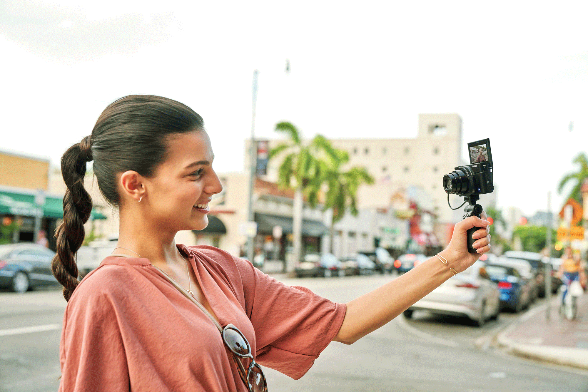 Woman holding a camera, vlogging on a street, sunny day.