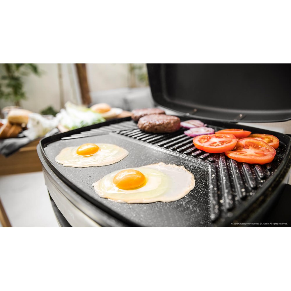 Una parrilla con huevos fritos, hamburguesas, rodajas de tomate y cebolla. Huevos en un lado, hamburguesas en el otro.