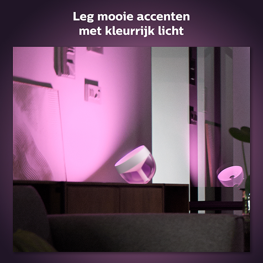 Room with pink-lit objects and a sofa. There are two lamps on a dark surface, and a painting.
