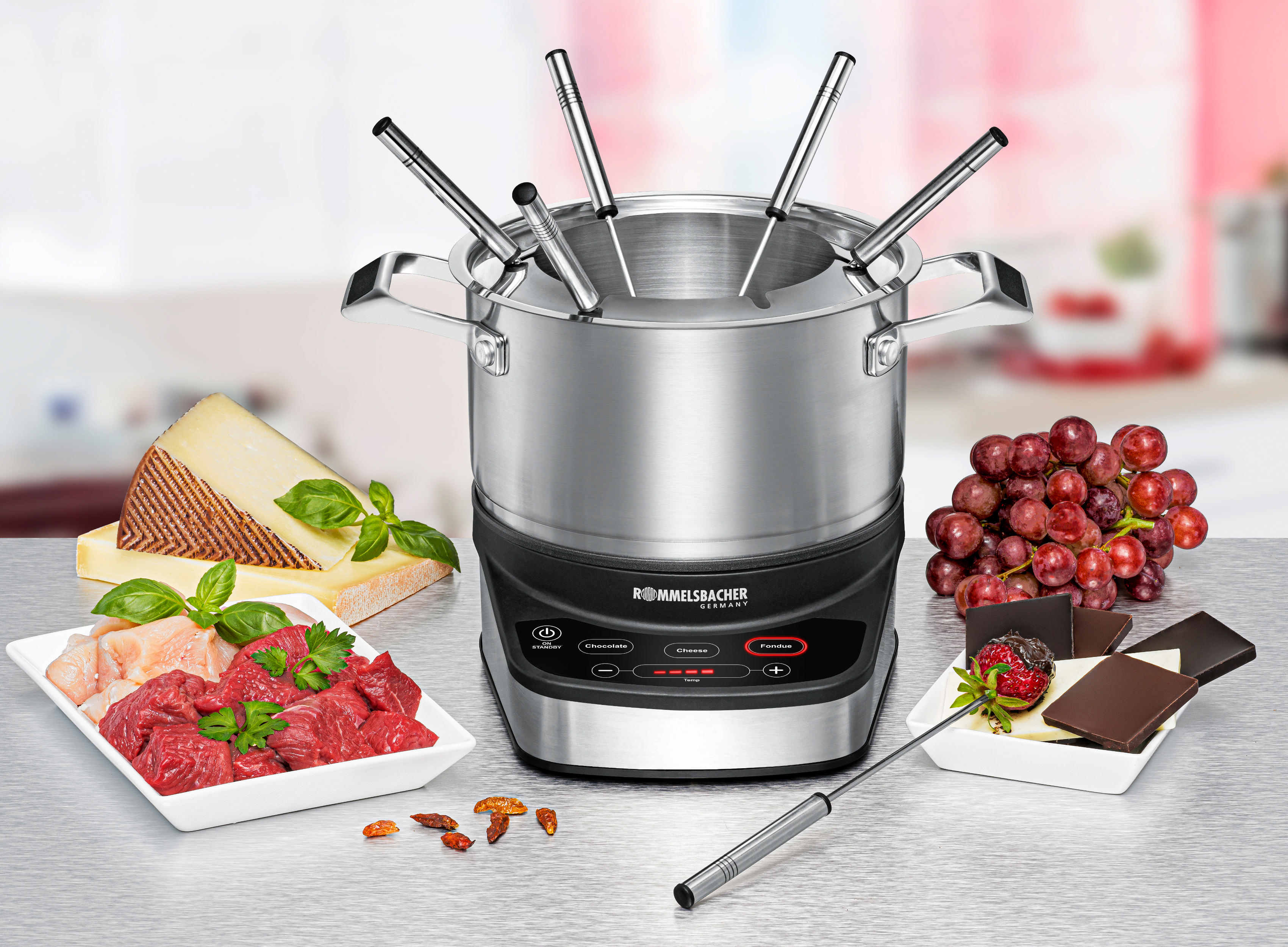 Fondue-Set mit Essen: Fleisch, Käse, Trauben, Schokolade und Erdbeeren auf einem Tisch.