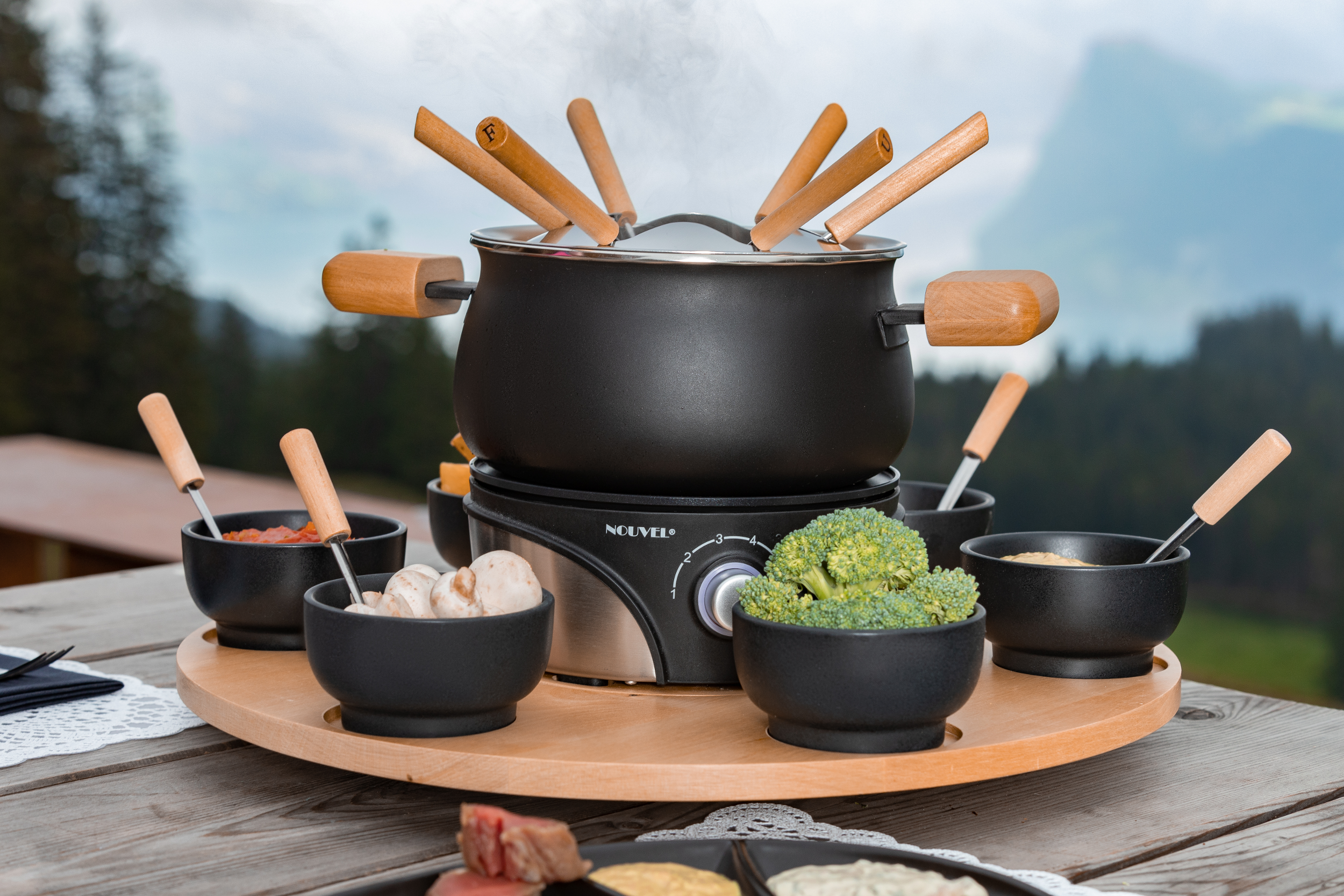 Set fonduta con pentola nera, manici in legno, ciotole di cibo, su tavolo.