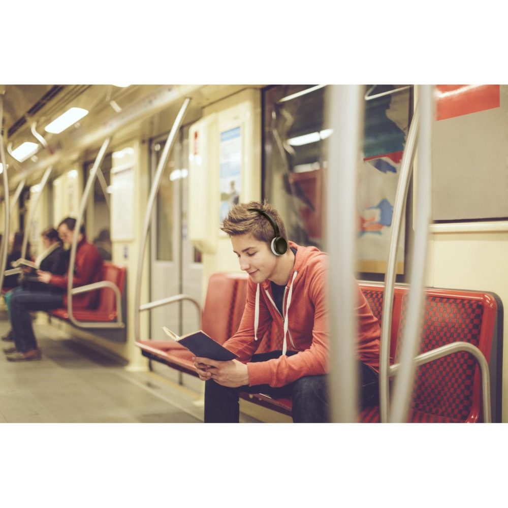 Un joven con auriculares leyendo un libro en un vagón de metro. El fondo tiene asientos.