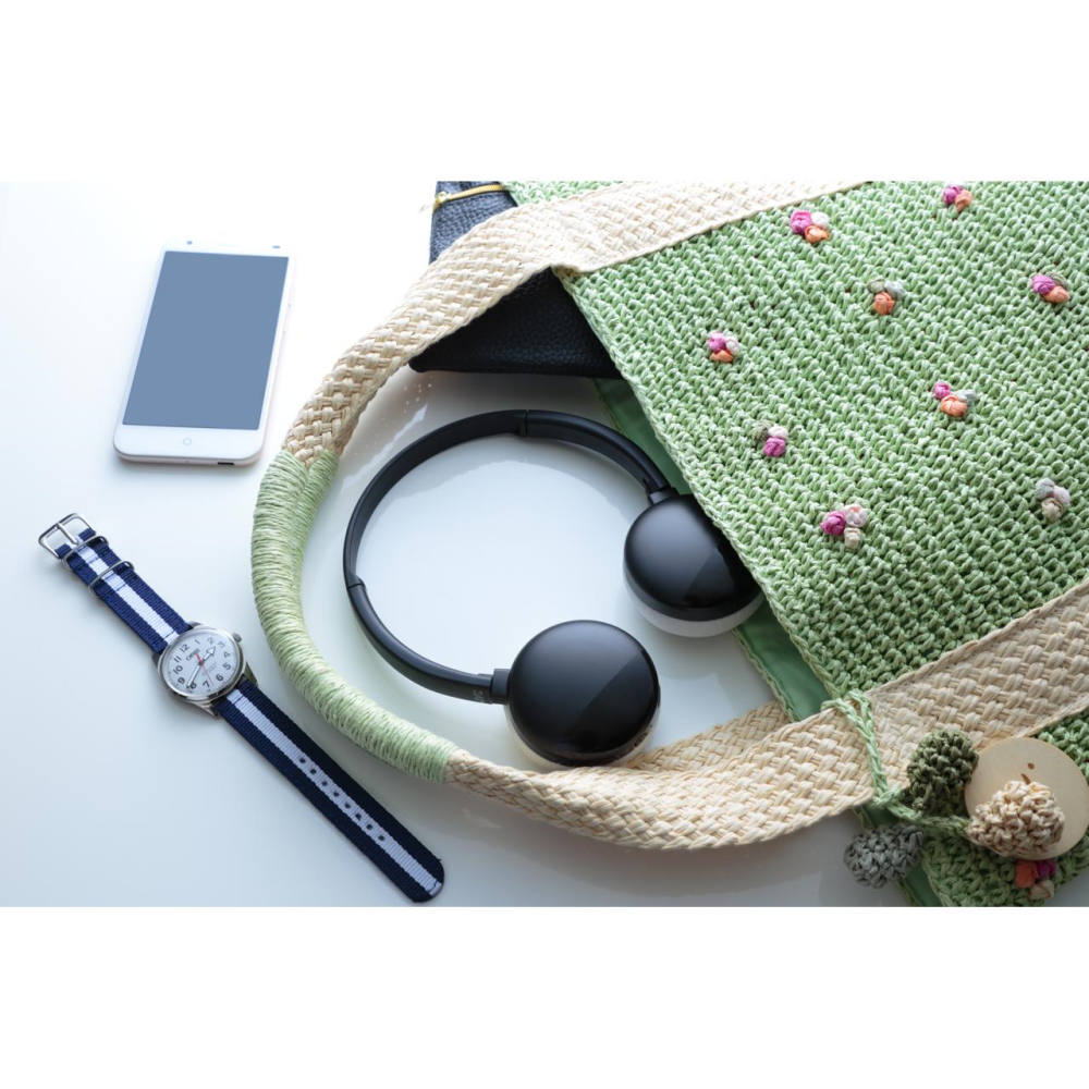 Teléfono, reloj y accesorios en una superficie blanca cerca de una bolsa verde.