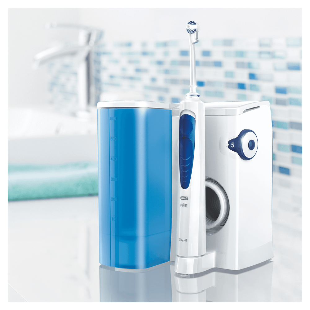 Un cepillo de dientes eléctrico, un irrigador dental y un depósito de agua sobre una superficie blanca de baño.